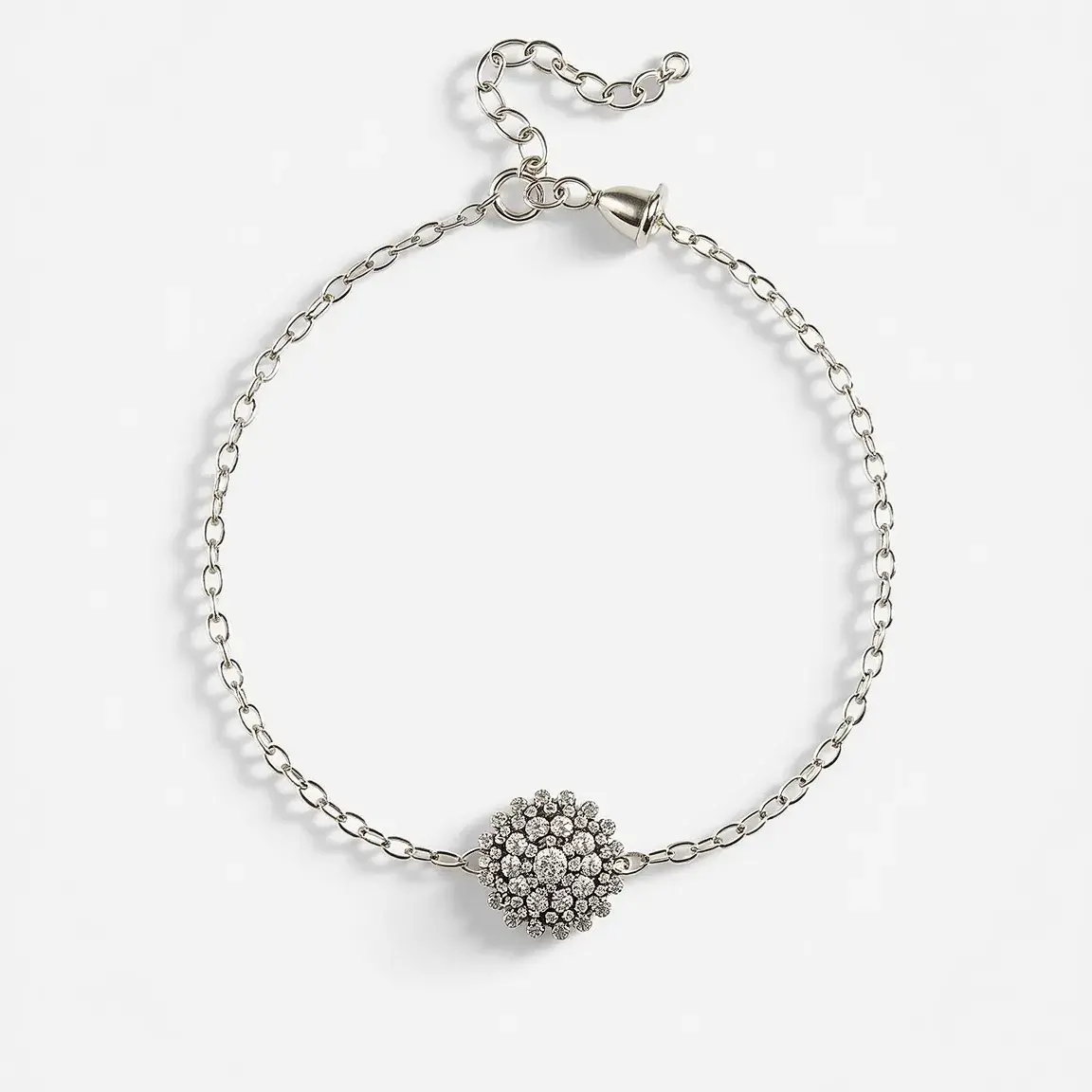 This ankle bracelet features a delicate chain made of silver-toned metal, adorned with a central large, spherical cluster of small, round, brilliant-cut clear gemstones, likely cubic zirconia, set closely together to create a sparkling focal point. The gems are secured in what appears to be prong settings, enhancing their brilliance and ensuring they catch the light from various angles. The bracelet is equipped with an adjustable chain extender and a lobster clasp, allowing for a customized fit and ease of use.