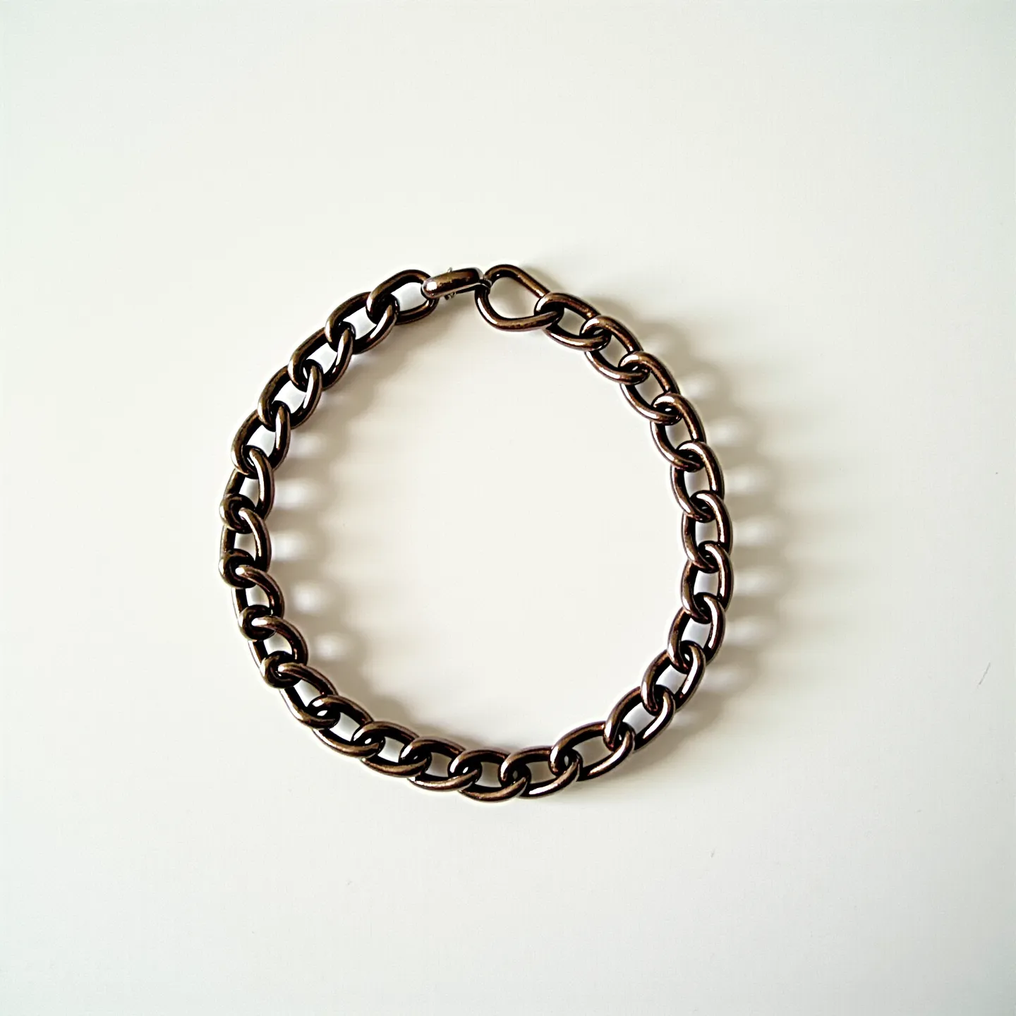 This ankle bracelet is composed of interlocking metal links that have a dark, polished finish. The design features a series of uniform, oval-shaped links creating a continuous chain that wraps around the ankle. It includes a simple yet secure clasp mechanism, consisting of a lobster claw clasp that attaches easily to a corresponding link. The bracelet appears crafted from a durable metal, adding to its strength and longevity.