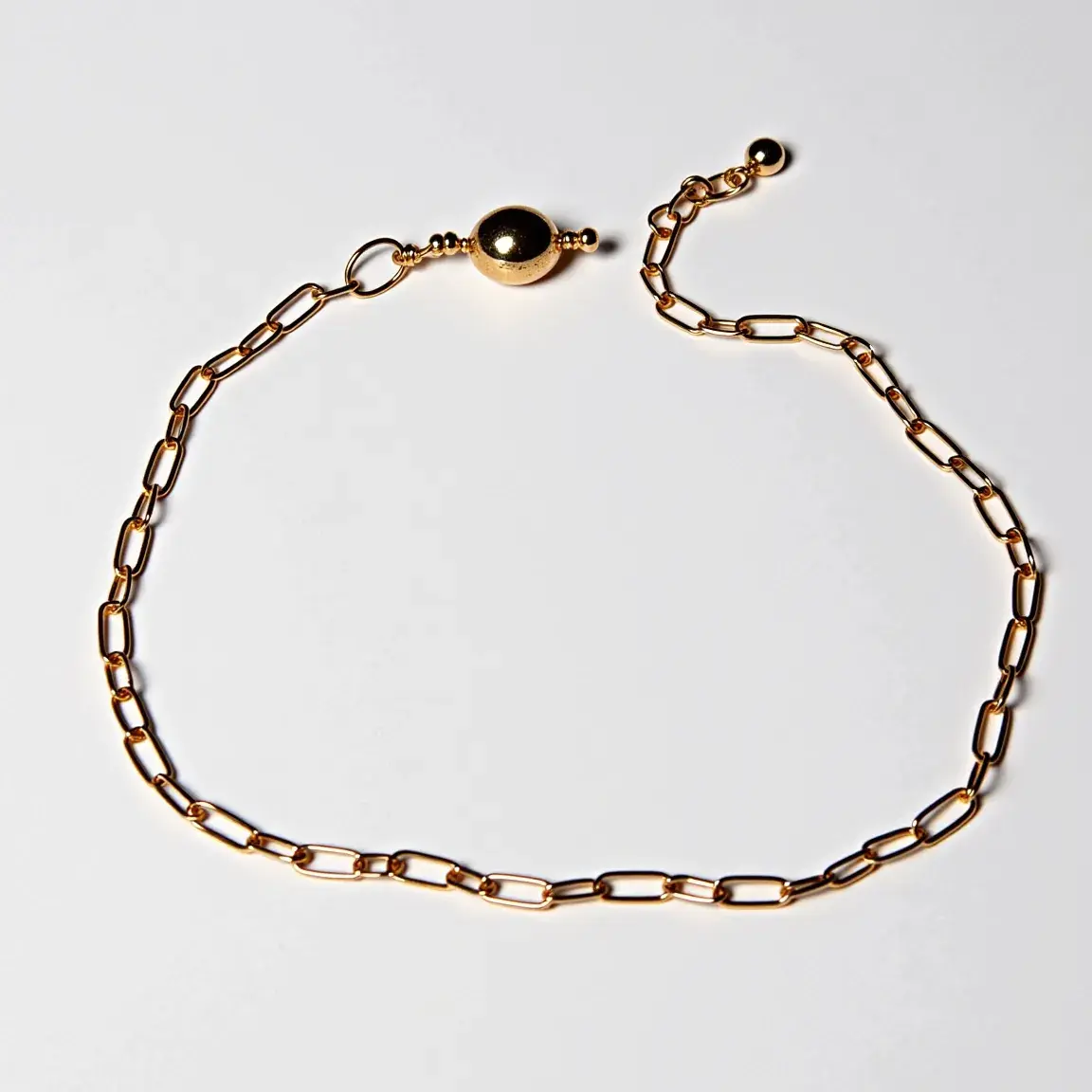 This ankle bracelet is crafted from a gold-toned metal and features a simple yet elegant design with elongated oval links that form the chain. It does not include any gem settings, making the design minimalistic and versatile. The bracelet is secured with a spherical magnetic clasp, which adds a subtle accent to the overall design, combining both functionality and style effortlessly.