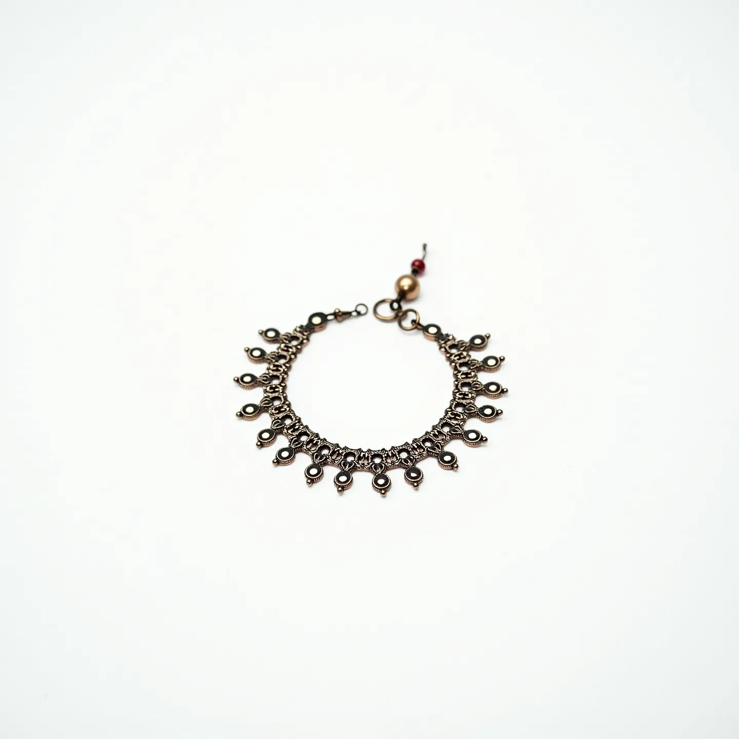 This ankle bracelet features a series of intricately linked metallic chains forming a delicate and ornate design. Encircling the chain is an array of small, teardrop-shaped metallic dangles, each attached to the bracelet via individual loops. At the end of the bracelet is a small clasp designed to secure the bracelet around the ankle, complemented by additional embellishments including a spherical bead and a small maroon bead attached to the clasp area. The overall craftsmanship highlights a balance of elegance and detailed metalwork.