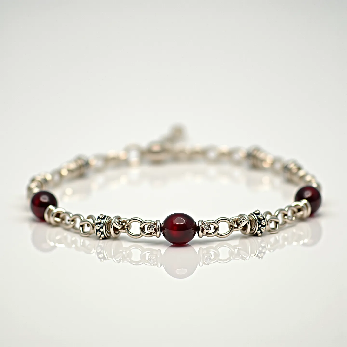 This ankle bracelet features a series of circular, deep red beads interspersed between ornate silver metal links. The red beads, which appear to be polished and almost translucent, are likely made of a gemstone such as garnet or carnelian, each one securely held in place by intricate silver bead caps on either side. The silver links between the beads are composed of interlocking rings, adding a decorative and sturdy structure to the bracelet. The clasp appears to be a simple but functional lobster clasp, providing a secure closure. The overall design is elegant with a balance of rich color and metallic brightness, making it a versatile piece that can complement various styles.