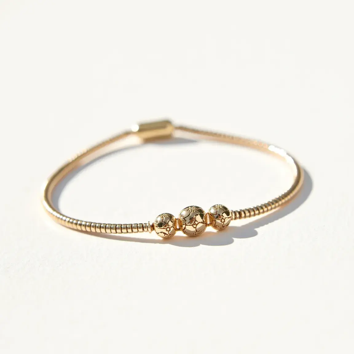 This ankle bracelet features a slender, flexible band that appears to be made of a gold-toned metal, giving it a lustrous and elegant appearance. It includes three round beads, each adorned with intricate cutout designs that add a touch of artistry and texture to the piece. The beads are symmetrically arranged, with the central one being slightly larger than the two flanking it, creating a balanced and aesthetically pleasing layout. The bracelet is secured with a metallic clasp that blends seamlessly with the overall design, ensuring both functionality and style. The minimalist yet sophisticated style of this ankle bracelet makes it a versatile accessory suitable for various occasions.