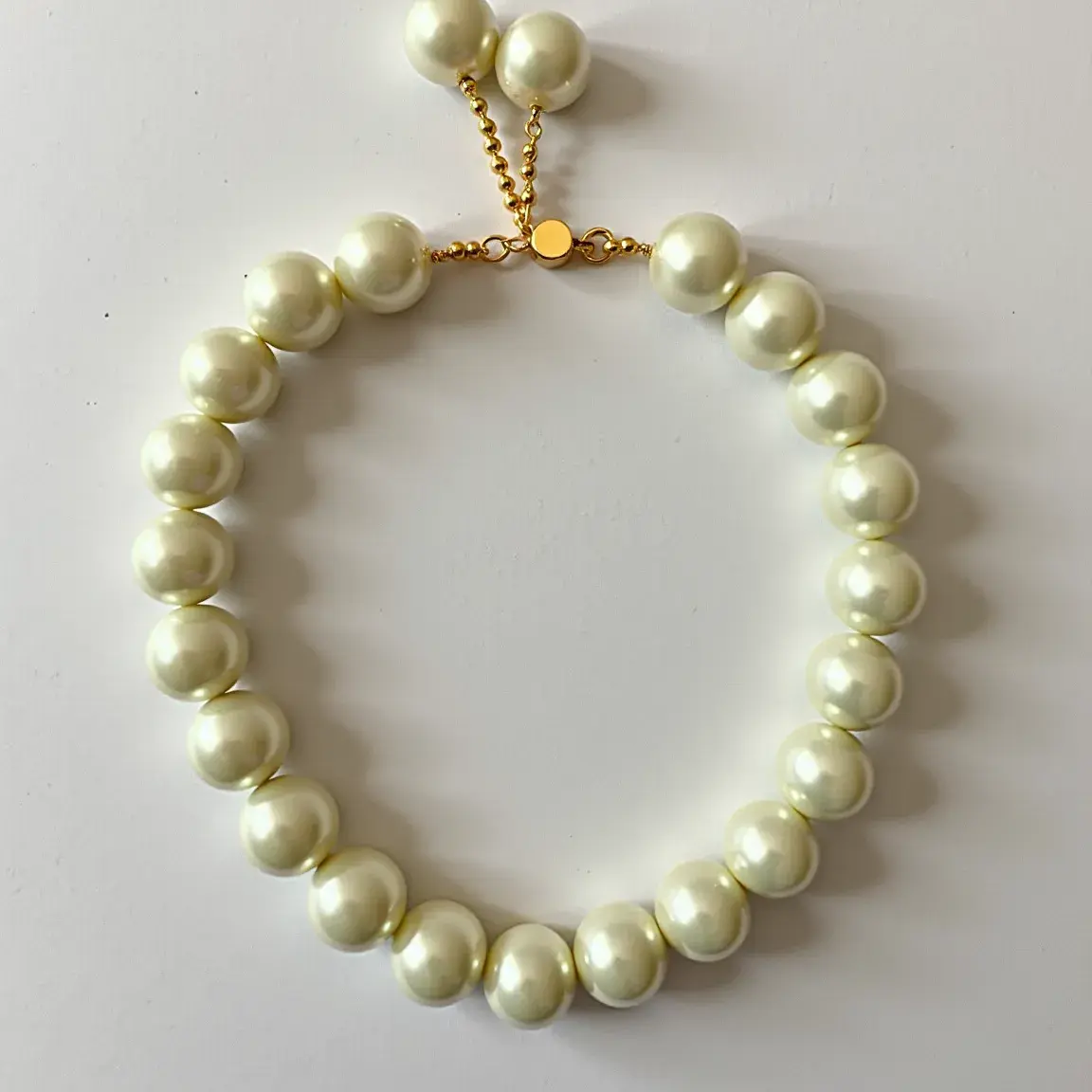 This baby bracelet features a delicate arrangement of round, lustrous pearls, likely simulated or cultured, strung together to form a charming and elegant accessory. The pearls are uniformly sized, contributing to a balanced and harmonious appearance. The bracelet is secured by a golden chain clasp, which includes a small circular plate, adding a subtle decorative element. Additionally, several pearls are attached to the end of the chain, providing a decorative flourish and potentially an adjustable length feature. The combination of the smooth, reflective pearls and the golden clasp enhances the overall aesthetic, making it suitable for special occasions or cherished as a keepsake.