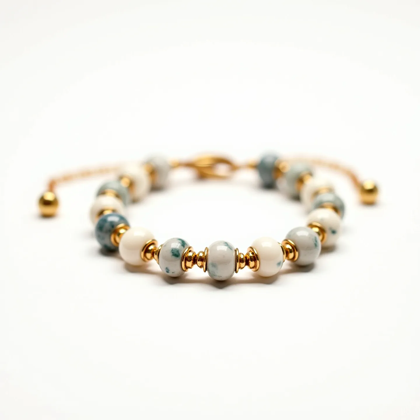 This baby bracelet features a charming arrangement of small round beads that likely include materials such as jade or painted ceramic stones, characterized by their pastel shades of green, gray, and cream. Each bead is separated by gold-toned spacer beads, adding a touch of elegance and contrast to the overall design. The bracelet appears to have a polished finish, enhancing its visual appeal. It is secured with an adjustable clasp mechanism, likely made of a metal alloy with a gold-tone finish matching the spacer beads, ensuring both functionality and style.