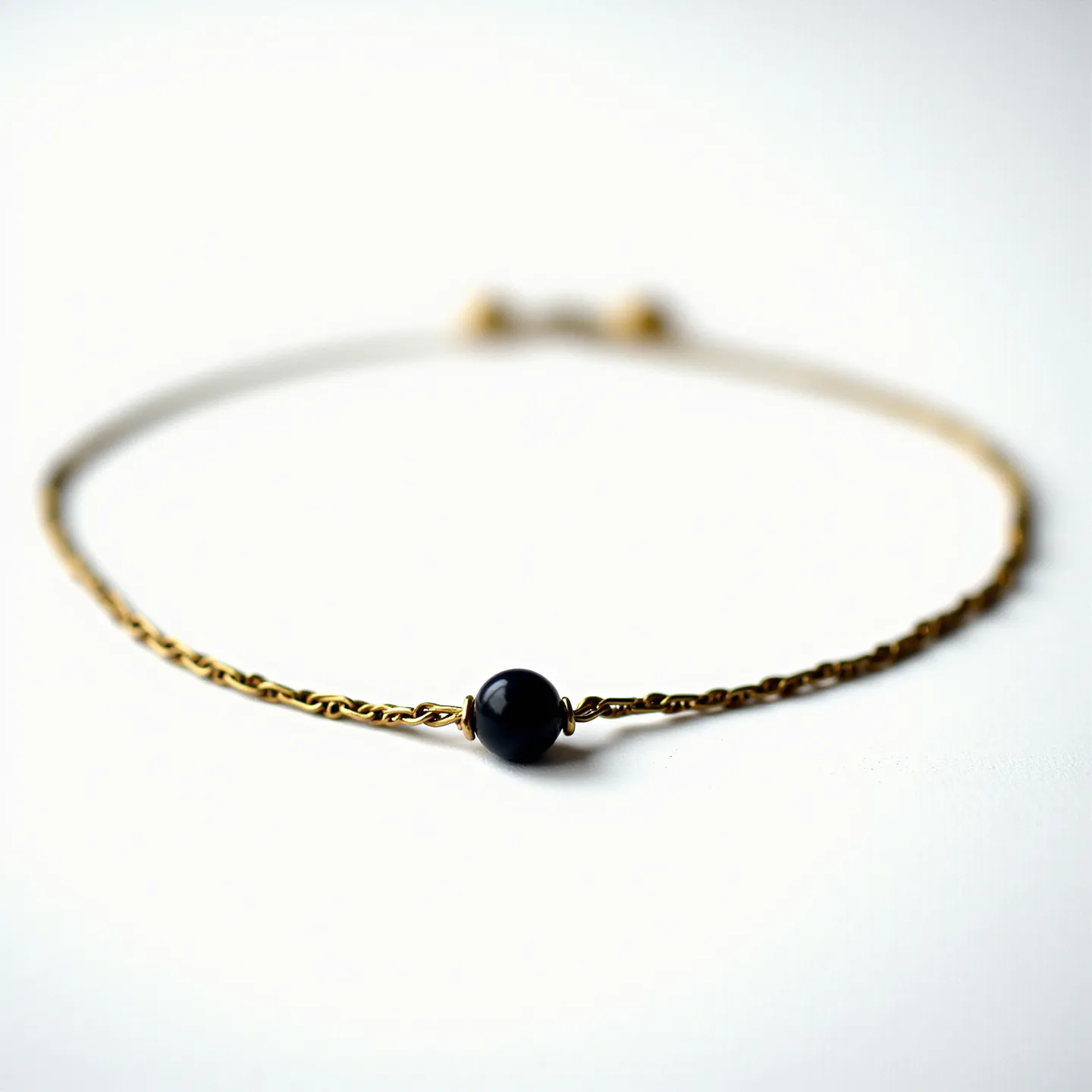 This baby bracelet features a delicate gold chain with a single small, polished black gemstone at its center. The black gemstone, which appears to be rounded into a smooth bead, is set simply within the chain, highlighting its polished surface. The chain itself is lightweight, designed to be gentle on the baby's skin. The bracelet is secured with a small, adjustable sliding clasp, allowing for a snug fit on the baby’s wrist.