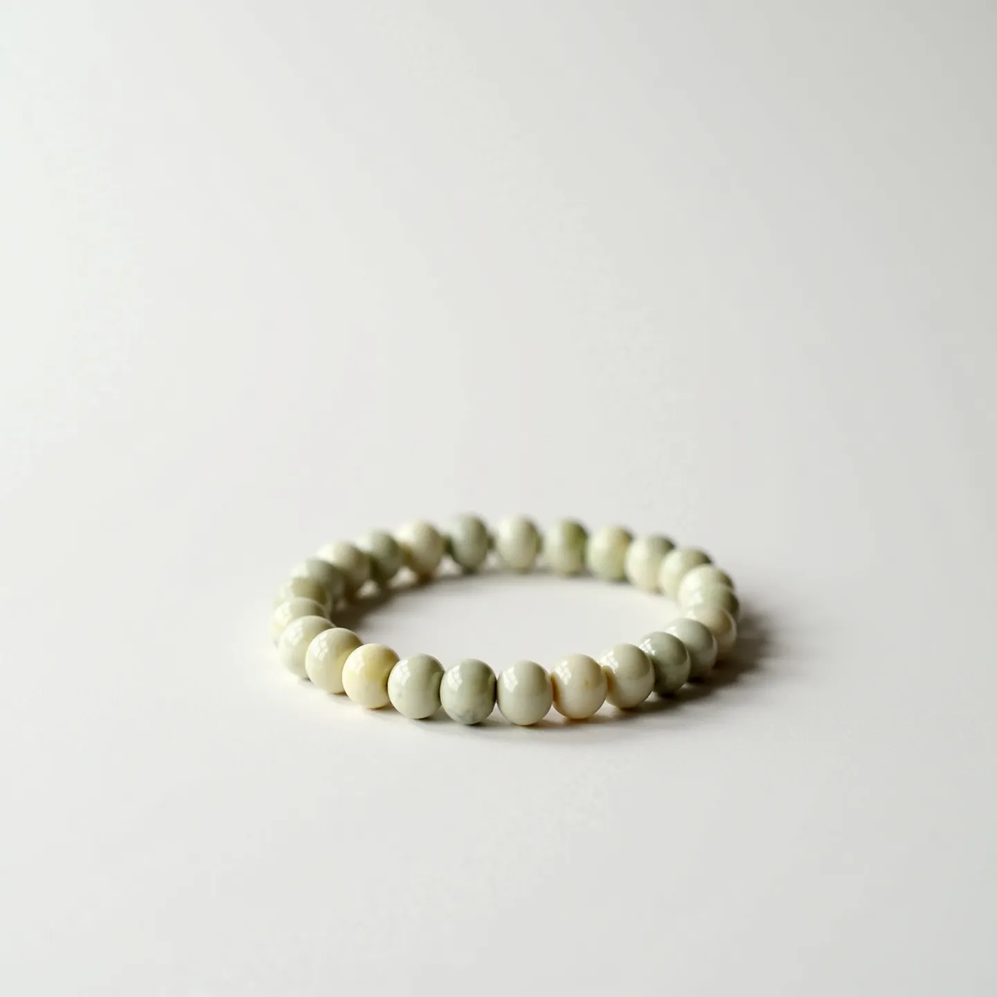 This baby bracelet consists of multiple smooth, round beads strung together to form a circular band. The beads appear to be made of a light-colored material, possibly a type of stone or mineral, with subtle variations in shading, ranging from creamy white to pale grey. The bracelet does not feature any distinct gemstones or metal settings, and the beads are uniformly sized and polished to a glossy finish. The bracelet is likely elastic, allowing it to stretch for easy wearing and removal, making it comfortable and practical for a baby.