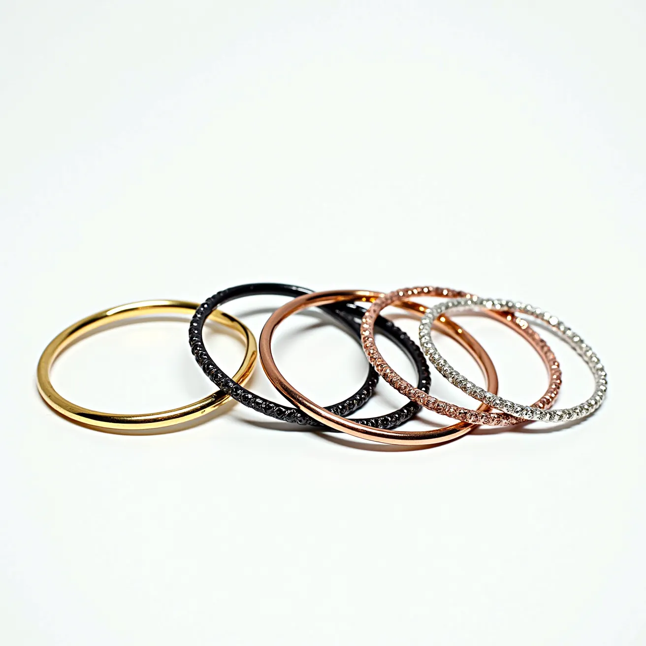 This bangles set features a variety of materials and finishes, showcasing a mix of metallic tones and intricate designs. The set includes a polished gold bangle, which provides a classic and elegant look. Another bangle is black with a textured surface or possible embedded gems that add visual interest. The collection also has rose gold bangles, one of which appears sleek and plain, while the other is adorned with clear, sparkling gems likely set in a prong or pave setting, giving it a more luxurious appeal. Additionally, there is a silver-toned bangle studded with similar clear gems, enhancing its shine and brilliance. There are no visible clasps or attachments, indicating that these are slip-on style bangles designed for easy wearing.