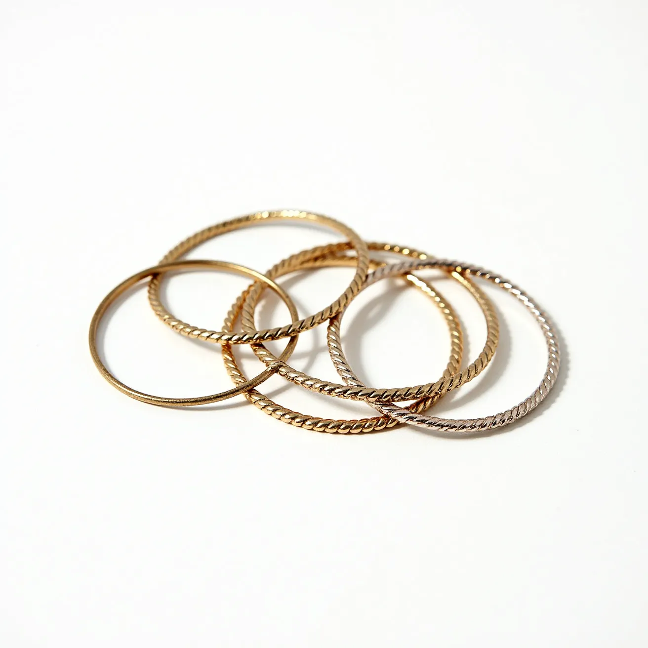 These bangles are crafted from metal, showcasing both smooth and twisted designs, likely made of gold or gold-toned alloy. The twisted bangles suggest a rope-like pattern, adding texture and dimension to the set. These bangles do not feature any gemstones or inset stones, focusing on a minimalistic, elegant appeal. The design is characterized by circular, continuous shapes without any visible clasps or attachments, indicative of slip-on bangles.