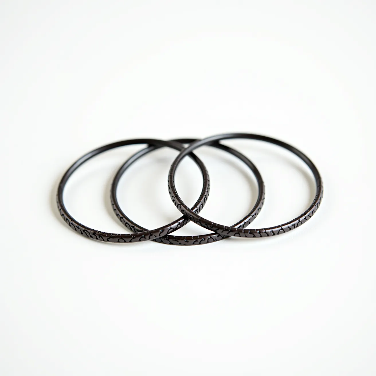 These bangles are crafted from a dark, possibly black material that features a textured, cracked pattern along the outer surface, giving them a unique and intricate appearance. The seamless circular design suggests a slip-on style, with no visible clasps or attachments. The uniform width and consistent design highlight the craftsmanship and attention to detail in their creation. Each bangle appears to be polished, contributing to their sleek and elegant look.