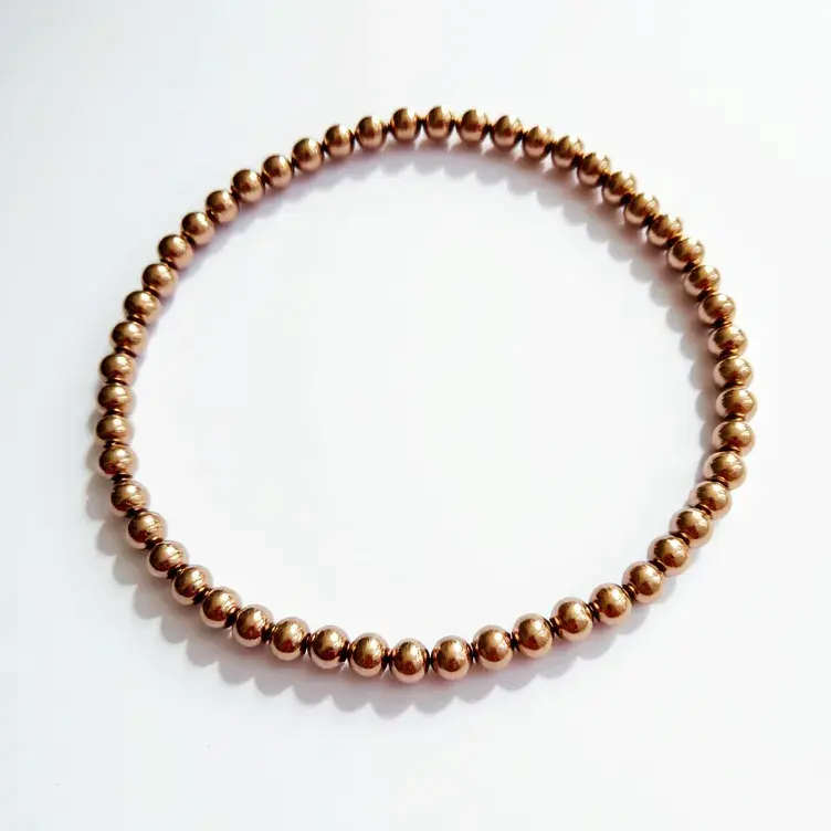 This beaded bracelet features a continuous arrangement of uniformly sized, spherical beads. Each bead appears to be made of a gold-colored material, giving the bracelet a polished and lustrous appearance. The spherical beads are meticulously strung together on what seems to be an elastic cord, allowing for flexibility and ease of wear. The bracelet lacks any visible clasp or attachment, suggesting that it is designed to be easily slipped on over the hand. The simplicity in its design emphasizes the uniformity and consistency of the beads, contributing to a cohesive and elegant aesthetic.