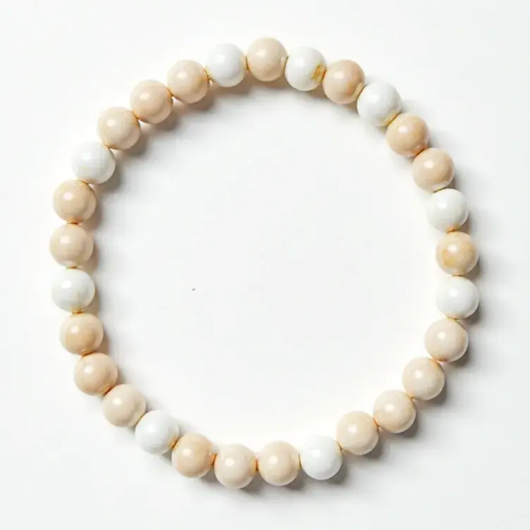 This beaded bracelet features alternating round beads crafted from smooth, polished material in soft beige and white tones. The beads are uniformly shaped, contributing to a balanced and aesthetically pleasing look. The bracelet is strung together seamlessly, creating an unbroken loop, likely on an elastic cord, as there is no visible clasp or attachment mechanism. The simplicity and elegance of the design highlight the natural beauty of the materials, making it a versatile accessory suitable for various occasions.