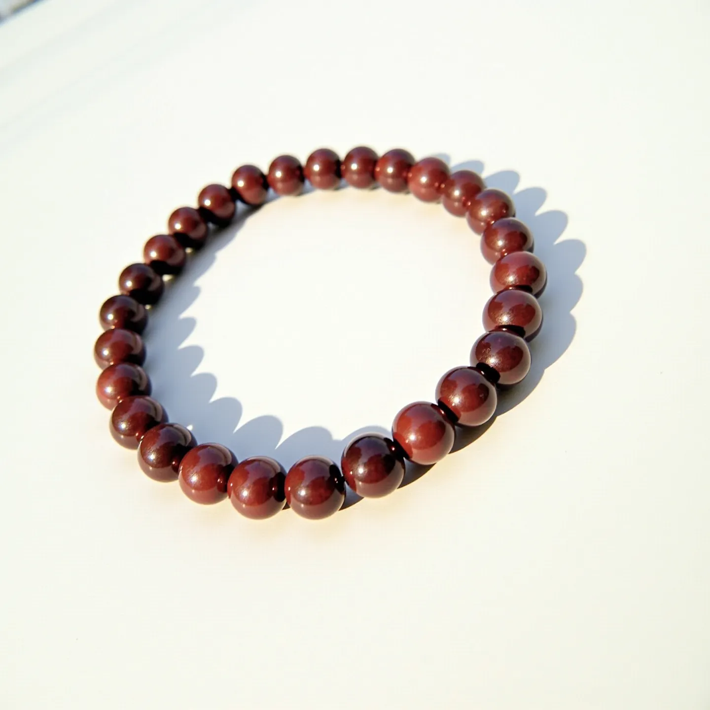 This beaded bracelet features a series of polished maroon beads strung together in a continuous loop. The beads appear to be round and uniformly shaped, suggesting they might be made from a natural gemstone or high-quality synthetic material. The bracelet does not seem to have a visible clasp, indicating it may be elasticated for easy wearing. The beads exhibit a glossy finish, enhancing their rich, deep red color and adding a touch of elegance to the overall design.