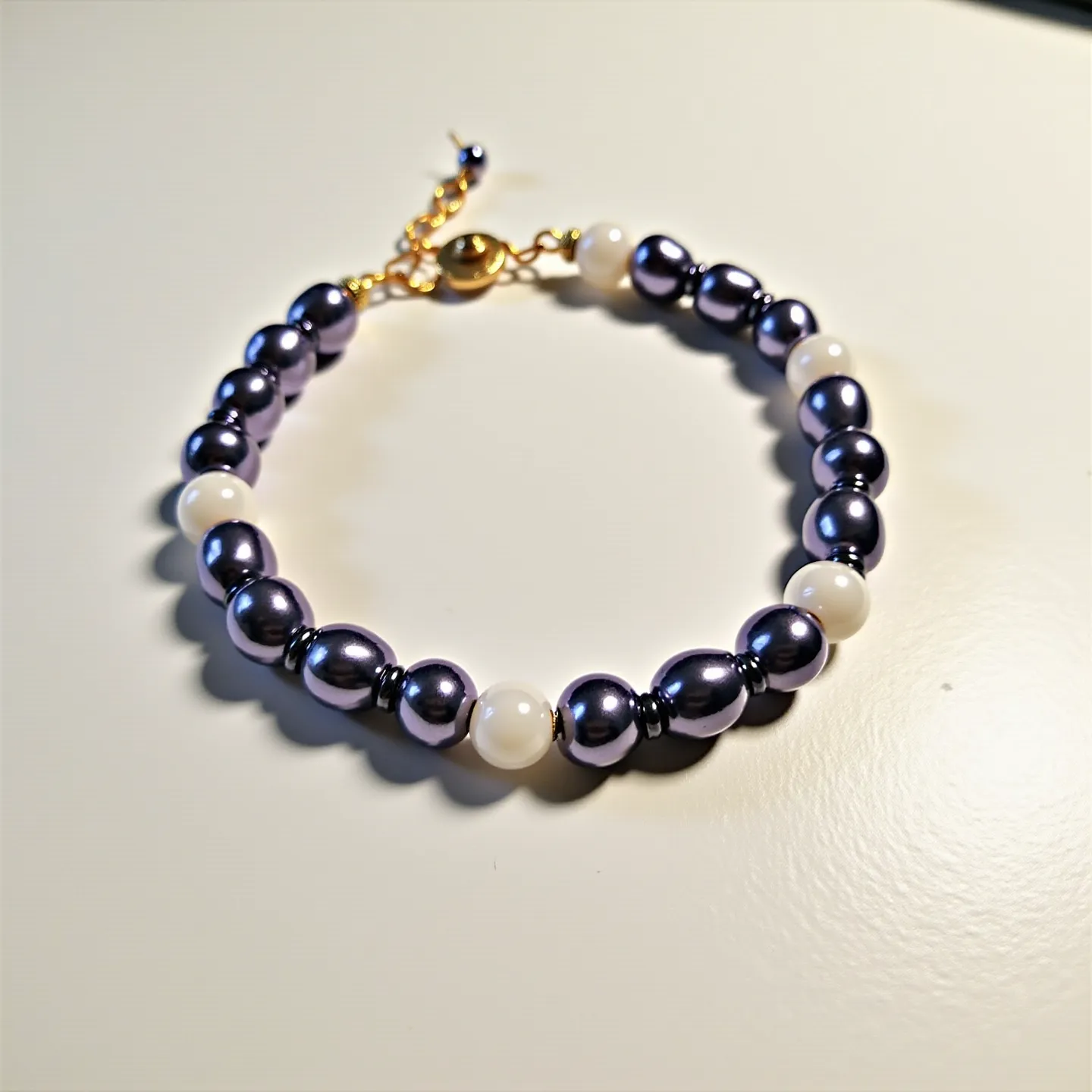 This beaded bracelet features a combination of lustrous black and white beads strung in an alternating pattern. The black beads appear to be oblong and polished, while the white beads are spherical and have a smooth finish. The bracelet is secured with a golden lobster clasp, which is attached to an adjustable chain allowing for size customization. The juxtaposition of the dark and light beads creates a visually appealing contrast, making this bracelet an elegant and versatile accessory.