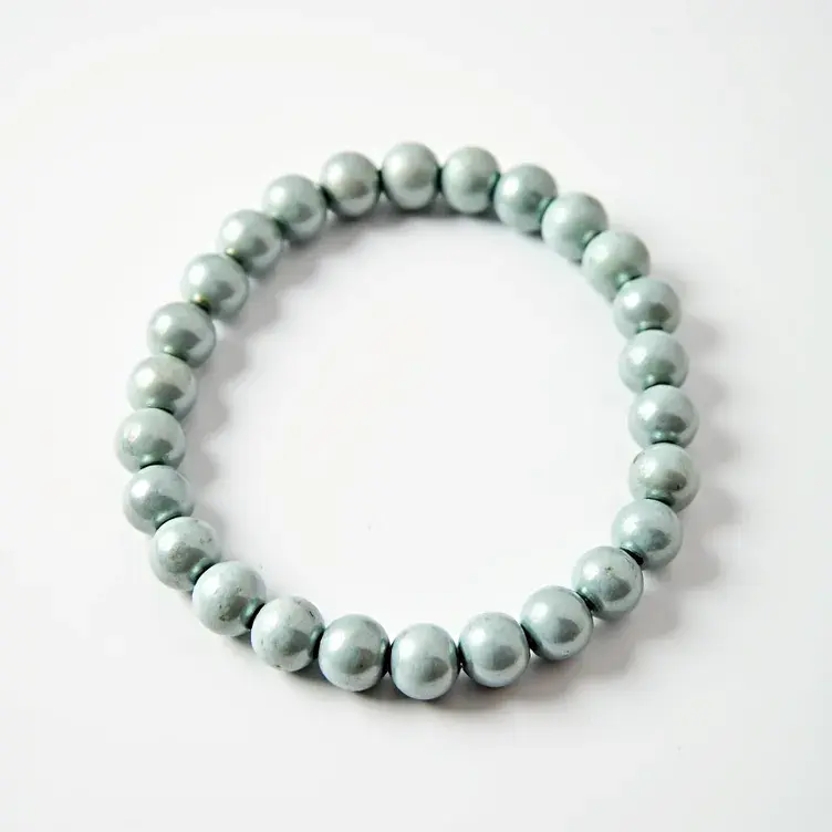 This beaded bracelet features a series of uniformly sized, smooth, and round beads. The beads appear to be a metallic or pearl-like gray color, giving them a lustrous sheen. The bracelet does not have a traditional clasp; it seems to be strung together on an elastic band, which allows it to stretch and fit over the wrist easily. There are no additional gems, stones, or settings visible on this bracelet, making it simple and elegant in design.