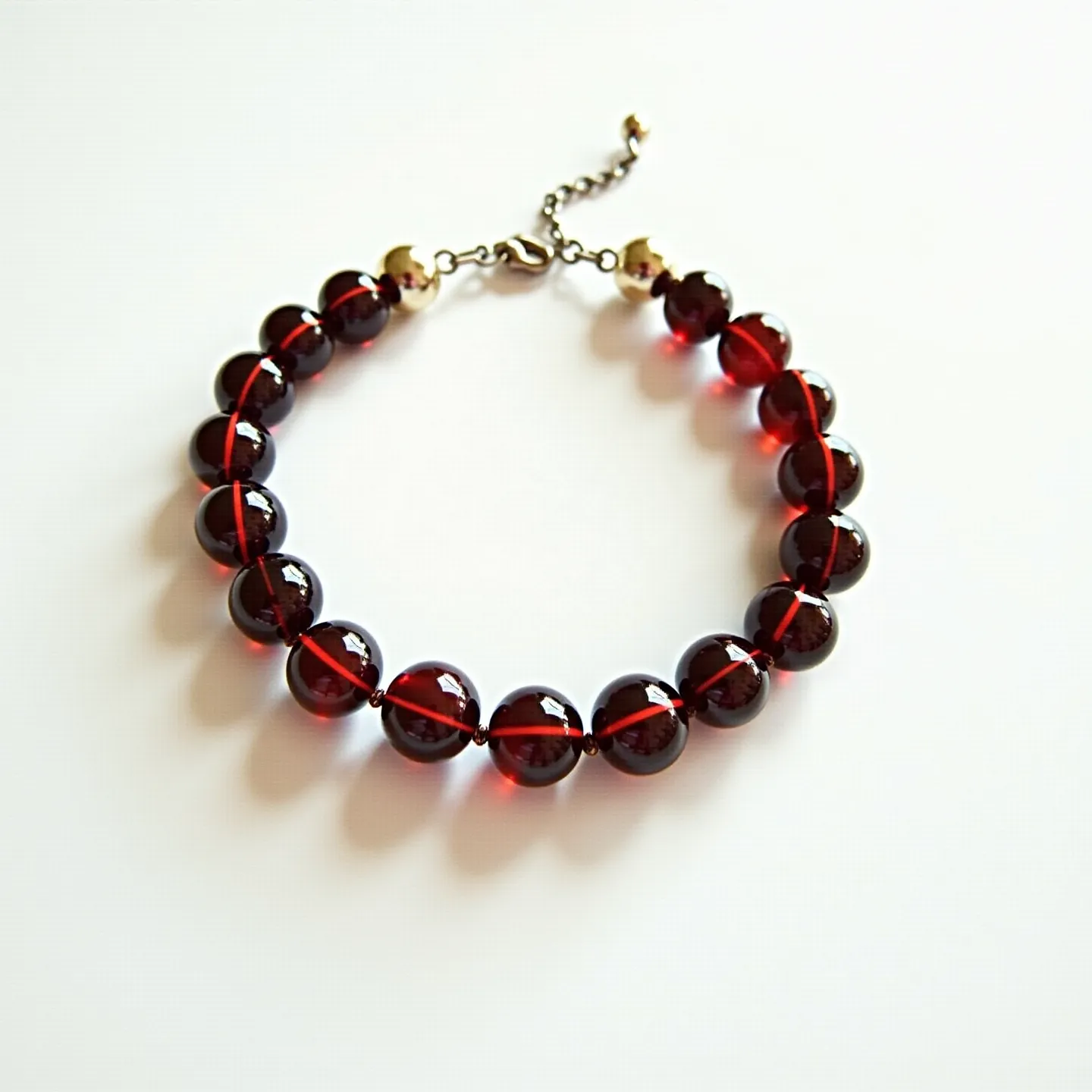 This beaded bracelet features a series of round, polished beads that give off a rich, deep red hue, likely indicating the use of garnet or another similar semi-precious stone. The beads are uniform in size and threaded together in a continuous strand, each separated by a small node that adds to the structural design. The bracelet is secured with a lobster clasp, which is attached to a short extension chain, allowing for adjustable sizing. The ends of the beaded strand are capped with small gold-toned beads, enhancing the overall elegance and providing a sophisticated finish to the piece.