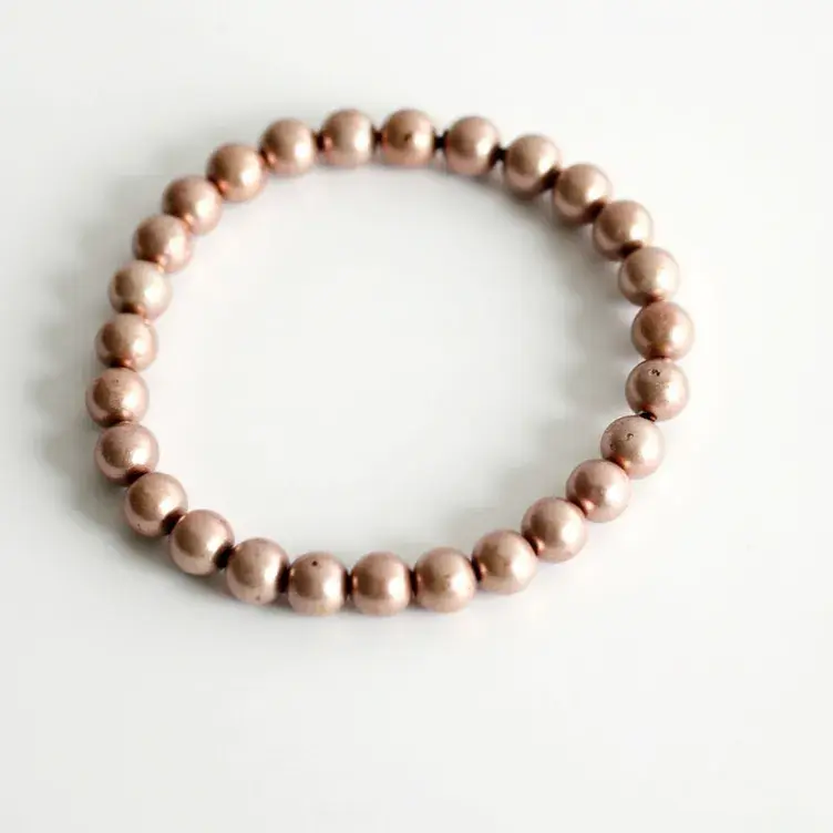 This beaded bracelet features a simple, elegant design composed of uniformly sized round beads. The beads appear to be made from a metallic material with a matte finish. There are no visible natural gemstones or complex settings, ensuring a cohesive and minimalist aesthetic. The bracelet is strung together on an elastic cord, allowing it to stretch for easy wearing and removal, without the need for a clasp or additional attachment.