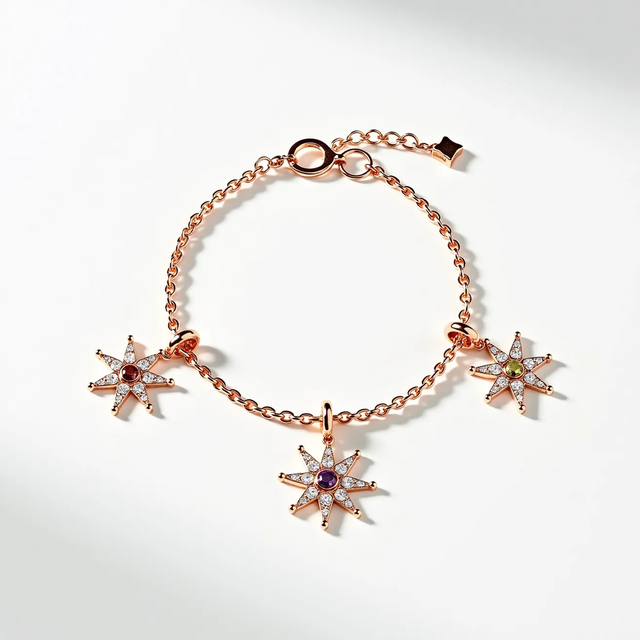 This charm bracelet features a delicate rose gold chain adorned with three star-shaped charms, each studded with various gemstones. The central elements of each star charm are a round-cut gemstone, in hues of red, purple, and green, set securely at the center. Surrounding these central stones are smaller, clear stones that accentuate the star shape, creating a sparkling and intricate design. The bracelet is fastened with a simple, rose gold spring-ring clasp that ensures both security and elegance.