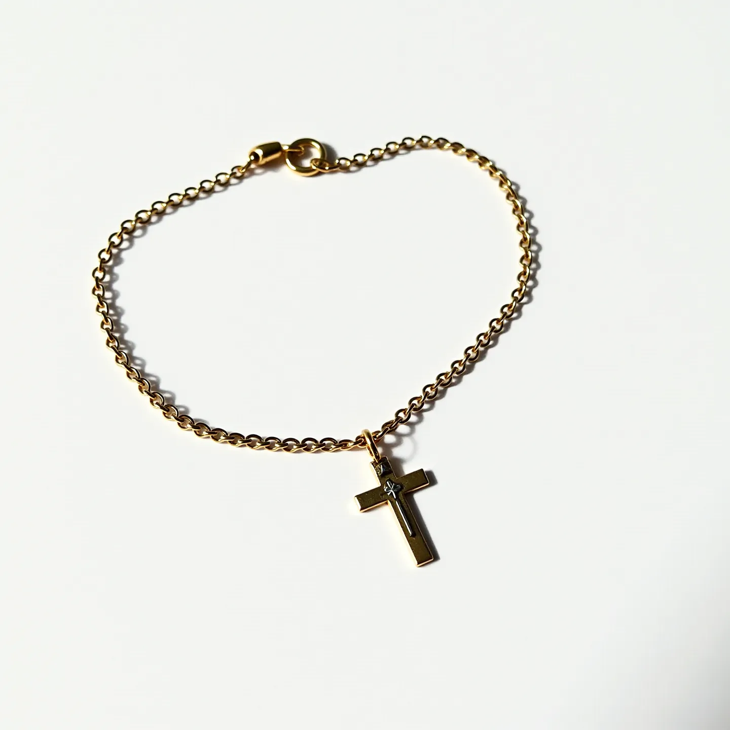 This cross bracelet features a delicate gold-colored chain linking to a small, polished cross pendant. The cross itself is adorned with a single gem set at its intersection, likely a small, round-cut diamond, securely held in what appears to be a bezel setting. The bracelet is equipped with a sturdy lobster clasp for secure attachment. The overall design exudes elegance and simplicity, making it a versatile piece that can complement various styles and outfits.