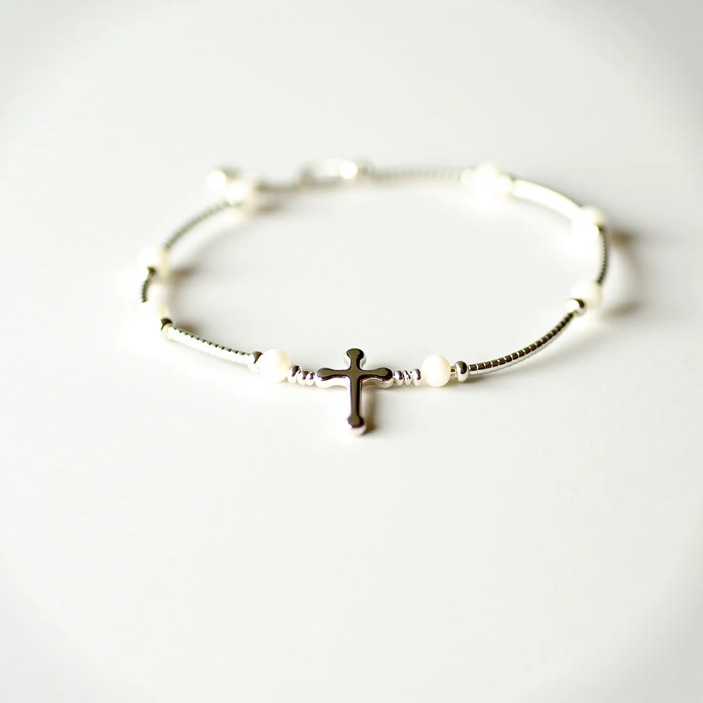 This cross bracelet features a delicate design with what appears to be a shiny, metallic cross at its center, which serves as the focal point. The bracelet is composed of alternating spherical white beads and small cylindrical metallic elements that contribute to its intricate and elegant appearance. The cross is likely made from a polished metal, possibly silver or stainless steel, adding a sleek and timeless charm to the piece. The spherical beads, which may be pearls or synthetic equivalents, are smoothly integrated into the design, enhancing its sophistication. Additionally, the bracelet is secured with a lobster clasp, ensuring a firm and reliable closure while maintaining its delicate aesthetic.