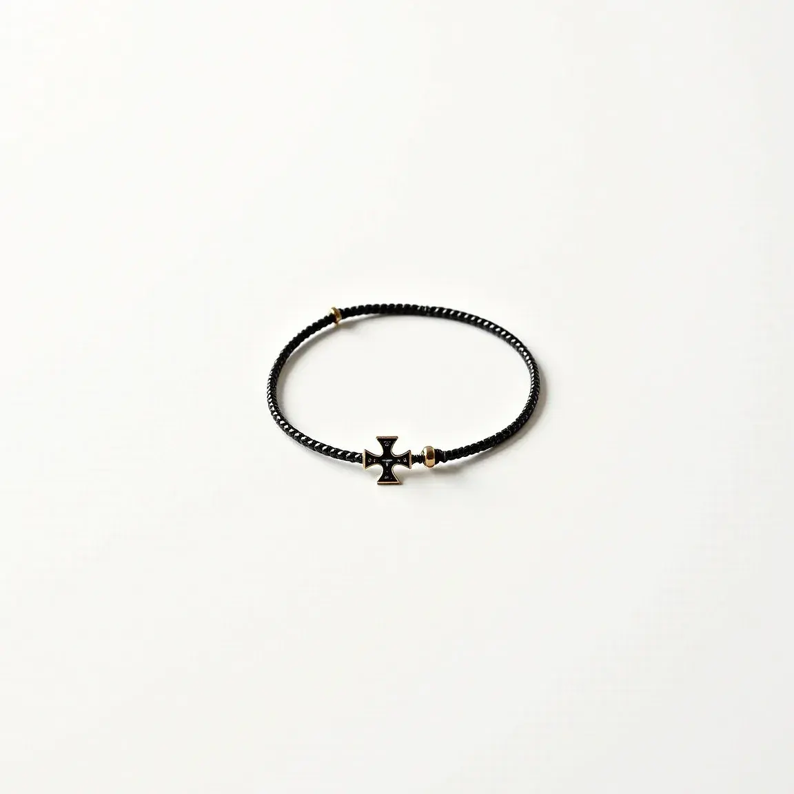 This cross bracelet features a braided black band complemented by a metal cross charm in the center. The cross has a distinct design with slightly flared edges and is accented with gold detailing. Adjacent to the cross, there are small gold beads that provide additional decorative elements. The bracelet appears to use a slip-knot or adjustable mechanism for fastening, allowing for a customizable fit. The combination of black and gold gives the bracelet a striking, elegant appearance suitable for casual and semi-formal wear.