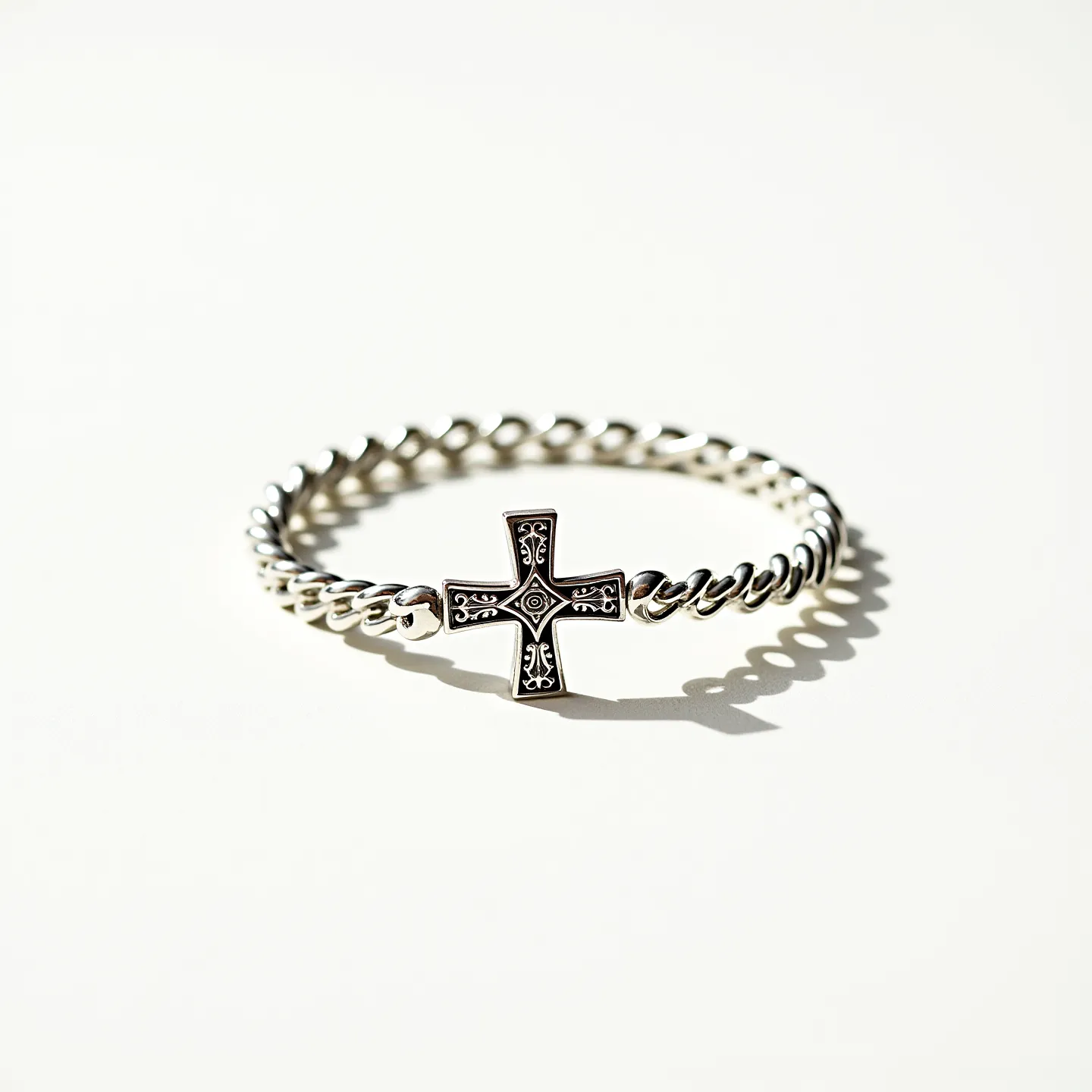 This cross bracelet features a decorative cross charm centered on a twisted metal chain. The cross is intricately designed with engraved patterns that give it a vintage or ornate appearance, and it is securely linked to the bracelet on both sides. The bracelet appears to be made of a polished metal, likely silver, given its shiny and reflective surface. There are no visible gems or stones set into the cross, and the bracelet does not appear to have a traditional clasp, suggesting it may be a continuous loop style.