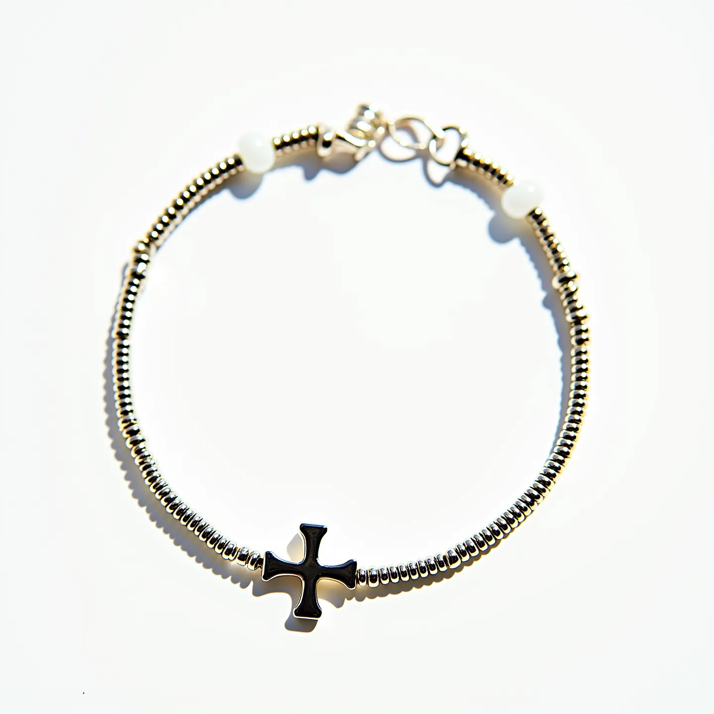 This cross bracelet features a central cross pendant made from a reflective, likely metal material, potentially stainless steel or similar. The bracelet itself is composed of a series of evenly sized, metallic beads strung together, lending a sleek and cohesive appearance to the piece. Additionally, there are two small spherical gems, possibly pearl or an opaque stone, incorporated into the design on either side, adding a subtle touch of elegance. The bracelet is fastened with a lobster claw clasp, ensuring a secure and adjustable fit for the wearer. This design blends simplicity with a classic aesthetic that is both modern and timeless.