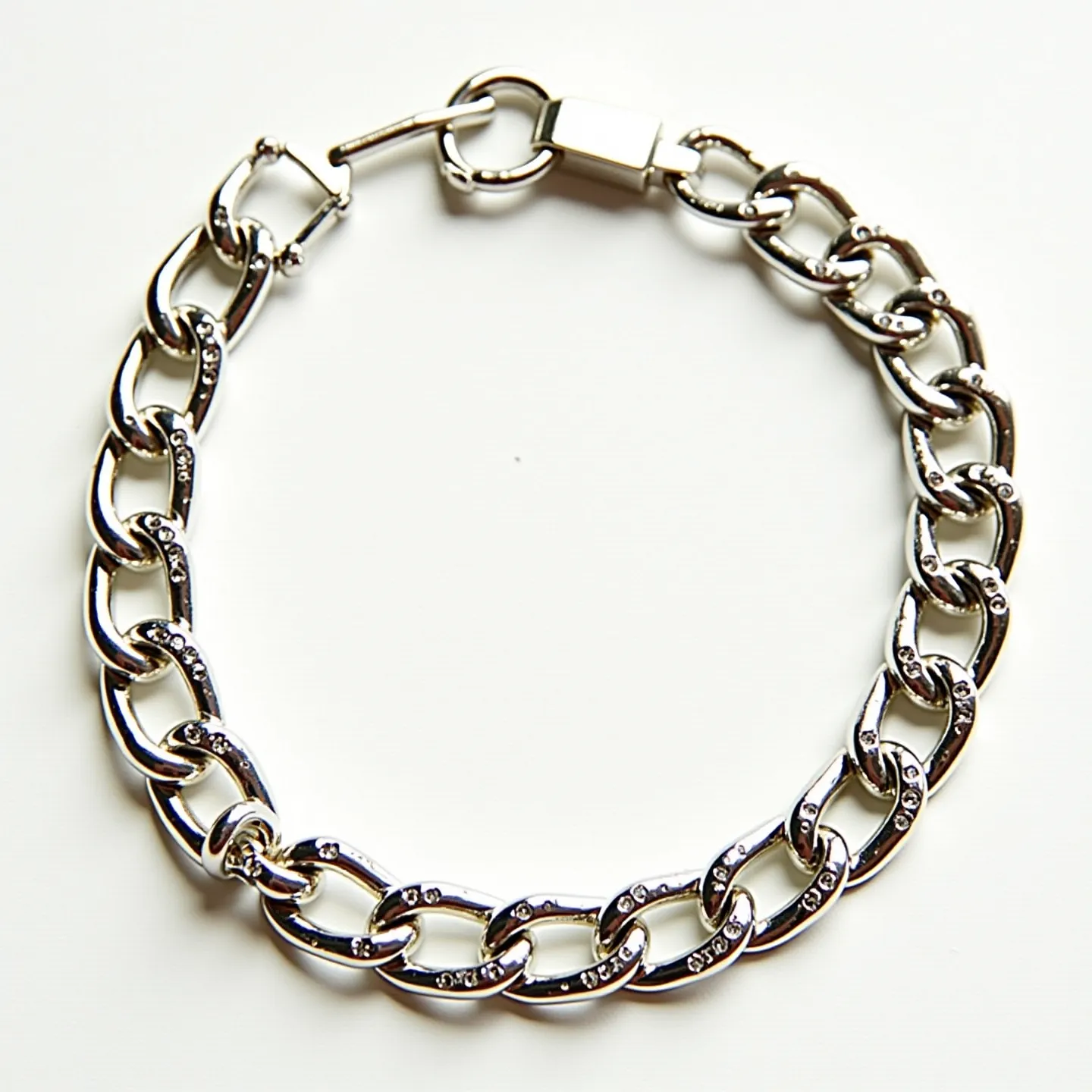 This cuban link bracelet features interlocking, oval-shaped links crafted from a polished metal resembling sterling silver or white gold. The links are adorned with small, round-cut stones that are likely diamonds or diamond-like gems, set using a pavé-style method which adds a touch of brilliance to the overall design. The bracelet is secured with a sleek and robust box clasp, ensuring both durability and ease of use for the wearer.