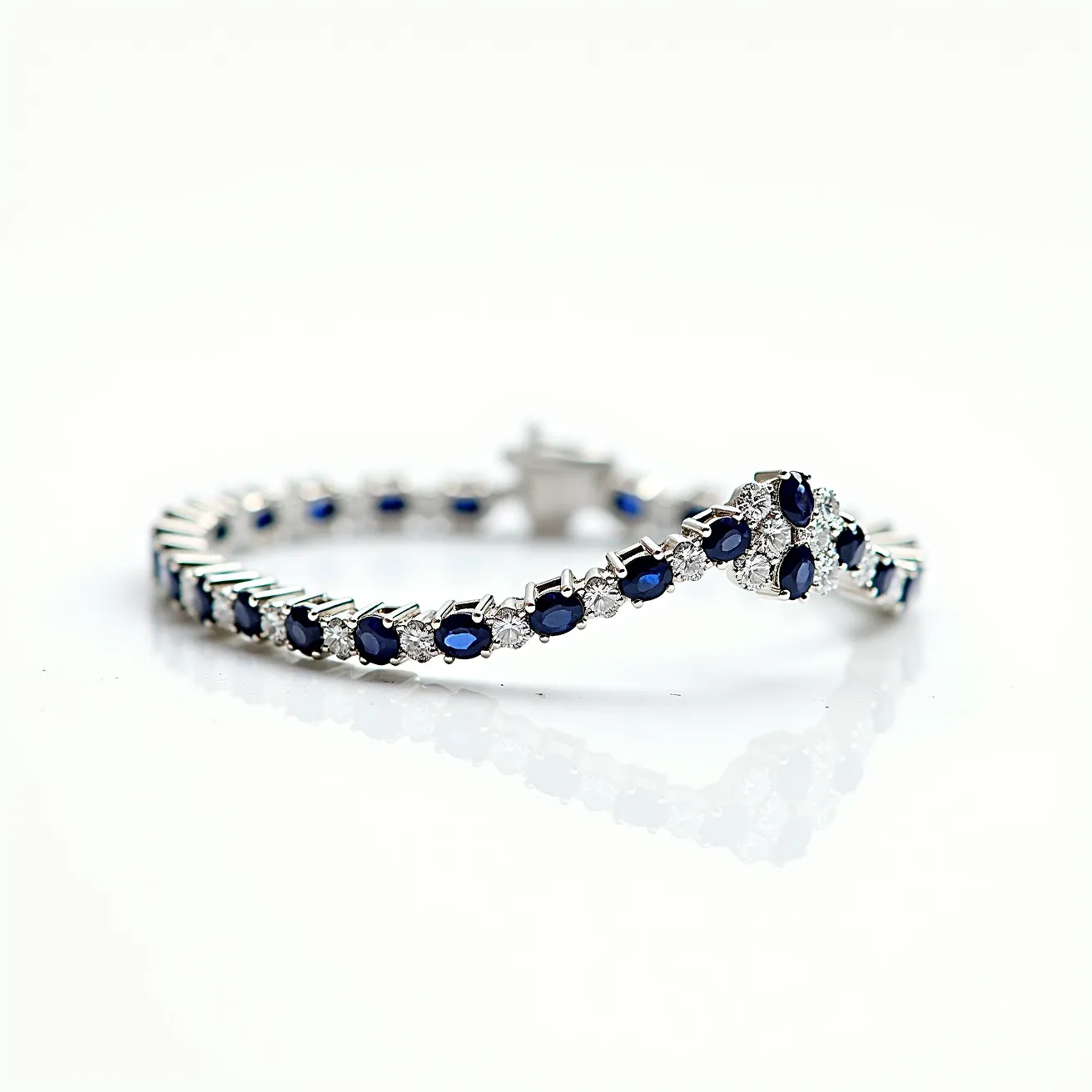 This diamond tennis bracelet is designed with alternating sets of gems. The primary gems are oval-cut blue sapphires, each encased in a four-prong setting, and they are interspersed with round-cut diamonds. The diamonds and sapphires are arranged in a single row, ensuring a seamless and elegant appearance. The bracelet features a box clasp with a safety latch for secure fastening. The materials used suggest the use of high-quality precious metals, most likely white gold or platinum, to enhance the brilliance and contrast of the gems.