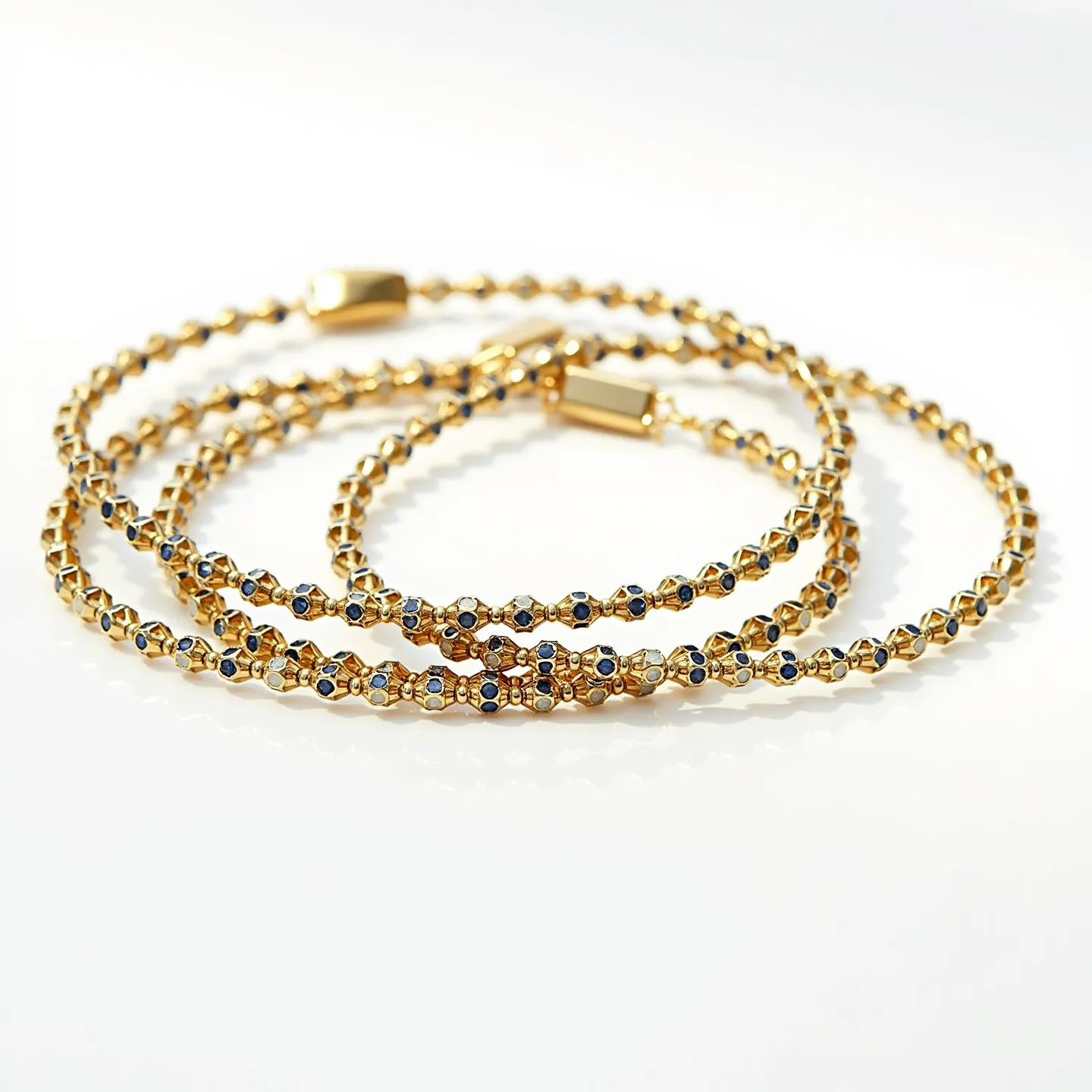 This gold beaded bracelet features a series of intricately linked, small, gold-toned beads that form the main structure, creating a delicate and elegant appearance. Interspersed among the gold beads are small, round, deep blue gemstones, possibly sapphires, which are uniformly set into the bracelet. The stones appear to be faceted, adding to their brilliance and enhancing the overall design. Each bead is intricately crafted, working harmoniously with the gemstones to provide a cohesive aesthetic. The bracelet employs a rectangular gold clasp, which ensures a secure closure and complements the overall design.