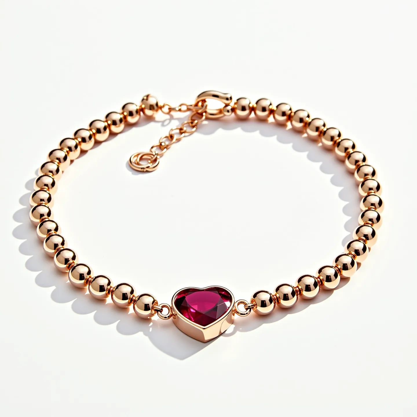 This gold beaded bracelet showcases a series of gleaming, spherical gold beads strung together to form an elegant and continuous loop. At its center, the bracelet features a heart-shaped gemstone, likely a ruby due to its deep red hue, which is set in a secure bezel setting that enhances its allure. The cut of the gemstone appears to be a faceted heart shape, adding sparkle and depth to the piece. The bracelet is fastened with a lobster clasp, ensuring a secure and adjustable fit, assisted by a small extension chain that adds both functionality and a slight decorative touch.