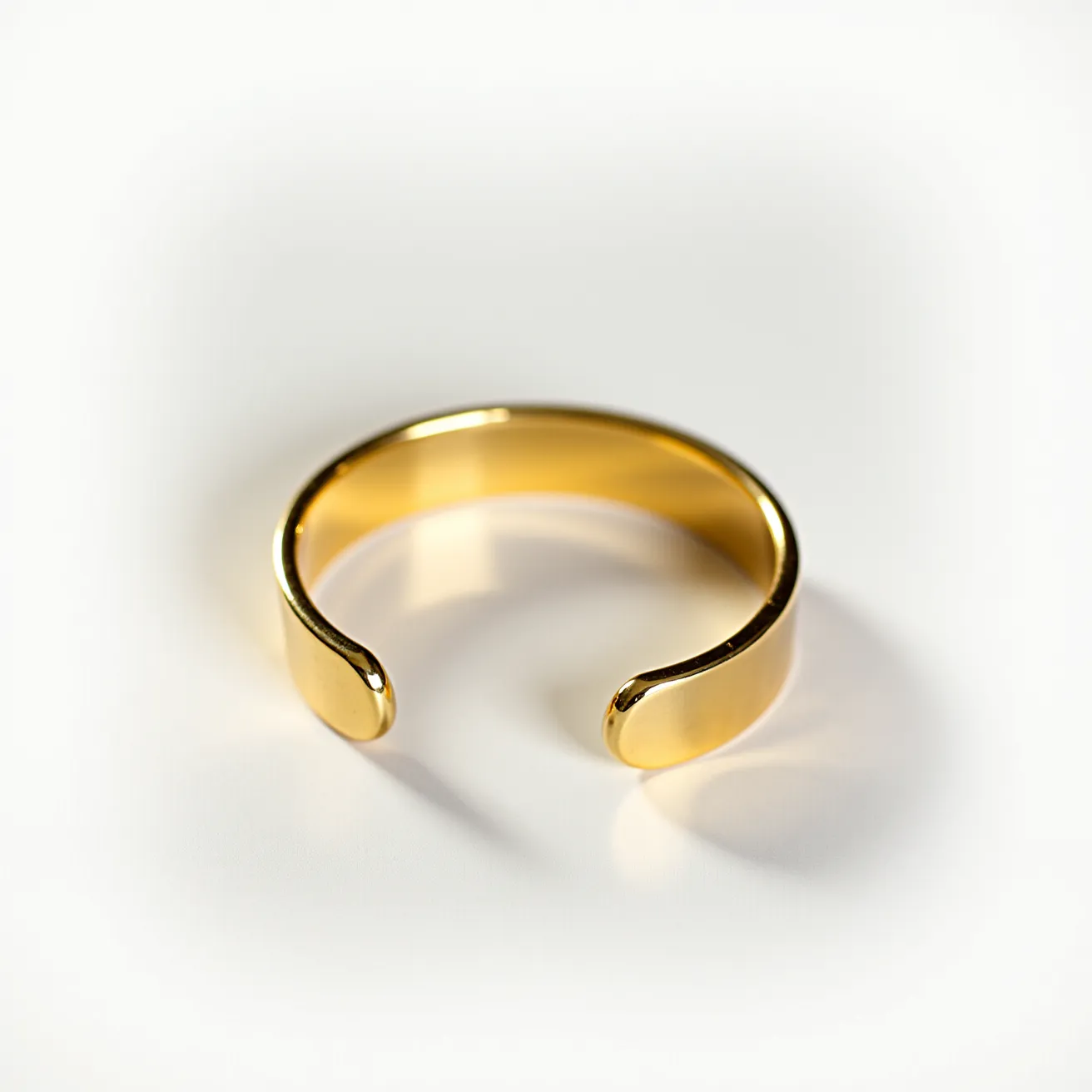 This gold cuff bracelet features a smooth, reflective surface made of polished gold metal. It is styled in a simple and elegant open-cuff design that allows for easy wearing and removal without the need for a clasp or other attachment mechanism. The bracelet does not feature any accompanying gems or stones, maintaining a clean and minimalist aesthetic. The ends of the cuff are rounded, adding to the comfortable and sleek appearance of the piece.