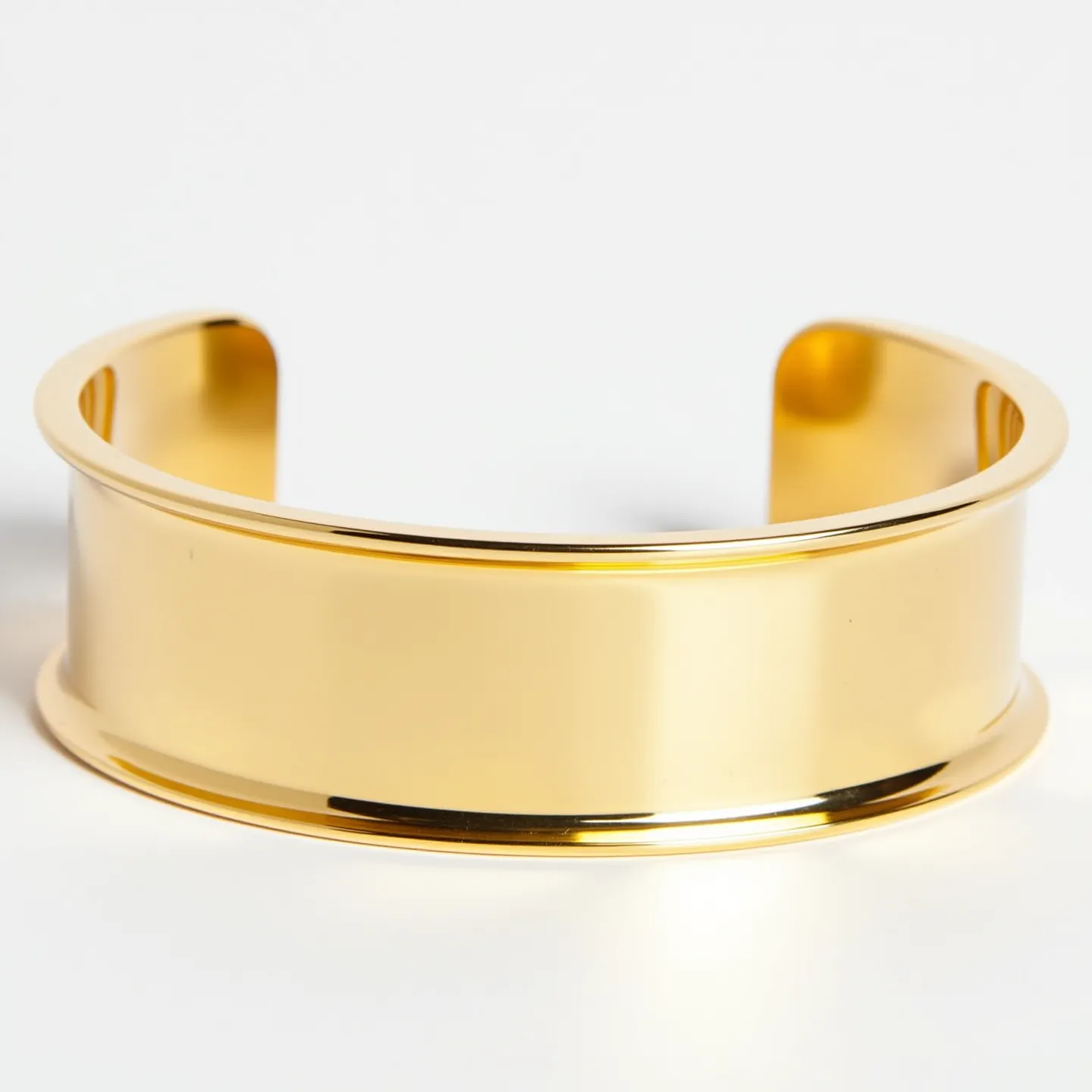 This gold cuff bracelet features a smooth, polished finish with a simple and elegant design. It is made of gold, exhibiting a rich and shiny appearance typical of the material. The bracelet is designed as a cuff, meaning it lacks a clasp or closure mechanism and instead relies on its open-ended shape to be worn on the wrist. The edges of the cuff are slightly rounded, adding a touch of refinement to the overall design. There are no additional gemstones, engravings, or decorative elements, allowing the gold's natural beauty to take center stage.