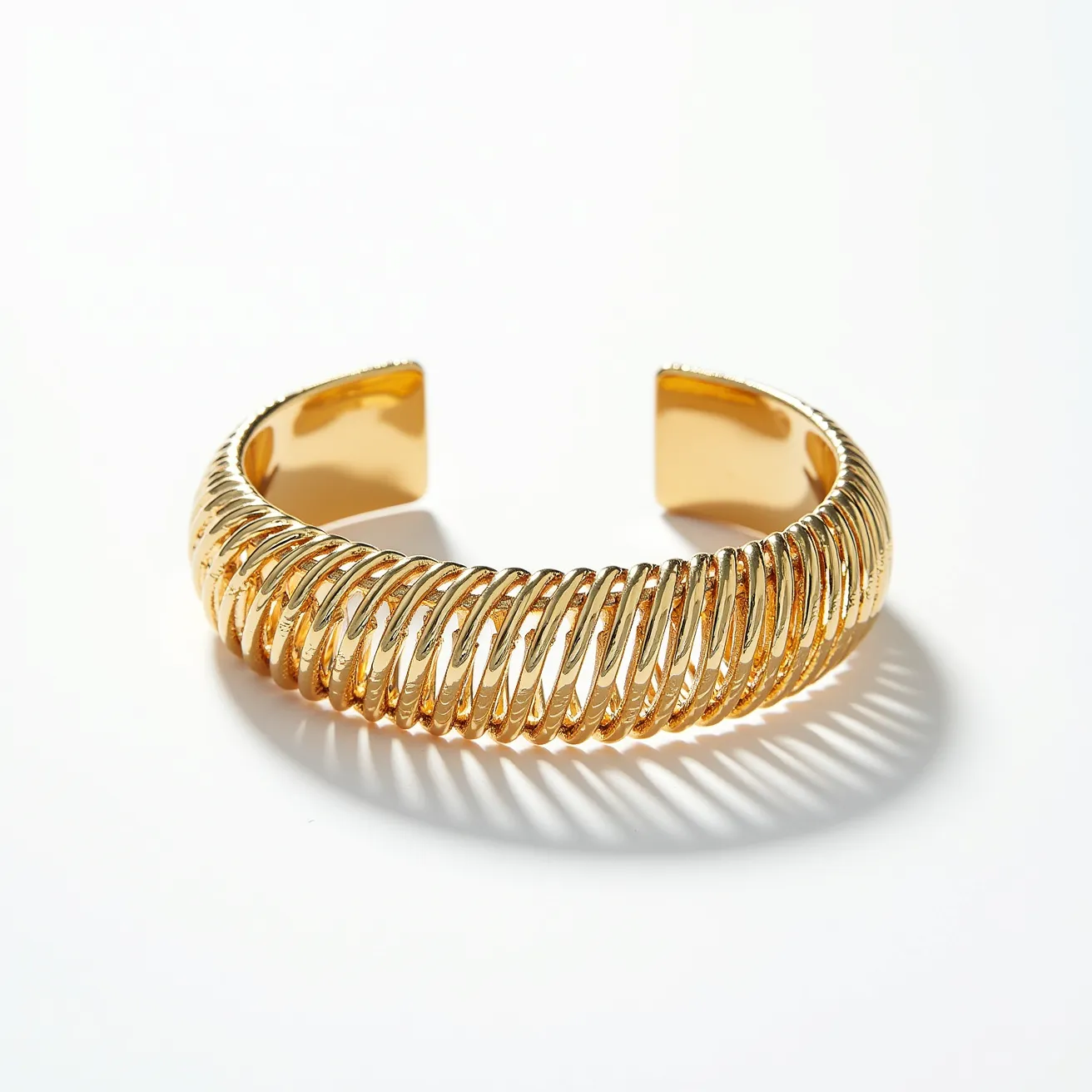 This gold cuff bracelet features a design of intertwined, looped elements that create a continuous, coiled appearance along its band. It is crafted from polished gold material, exhibiting a glossy, reflective surface that enhances its luxurious appeal. The open-ended design without any clasp allows for easy wearing and removal, and it is adjustable to fit various wrist sizes comfortably. The bracelet has an elegant and bold presence, suggesting a focus on intricate detailing and fine craftsmanship.