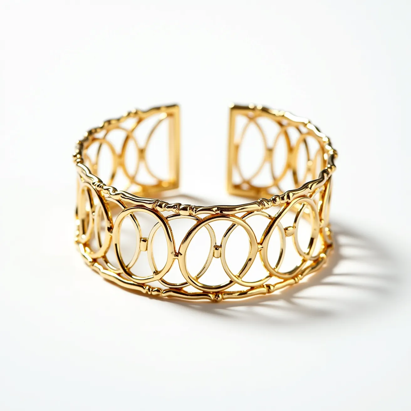 This gold cuff bracelet features a delicate design of interconnected oval loops, crafted from polished gold metal. The intricate pattern provides an elegant yet bold statement, with the open-frame structure allowing light to pass through, enhancing its luxurious appeal. The cuff design makes it easy to wear, as it slides onto the wrist without the need for a clasp or additional attachments. This timeless piece offers a sophisticated touch, ideal for both everyday wear and special occasions, with its smooth, glossy finish reflecting quality craftsmanship.