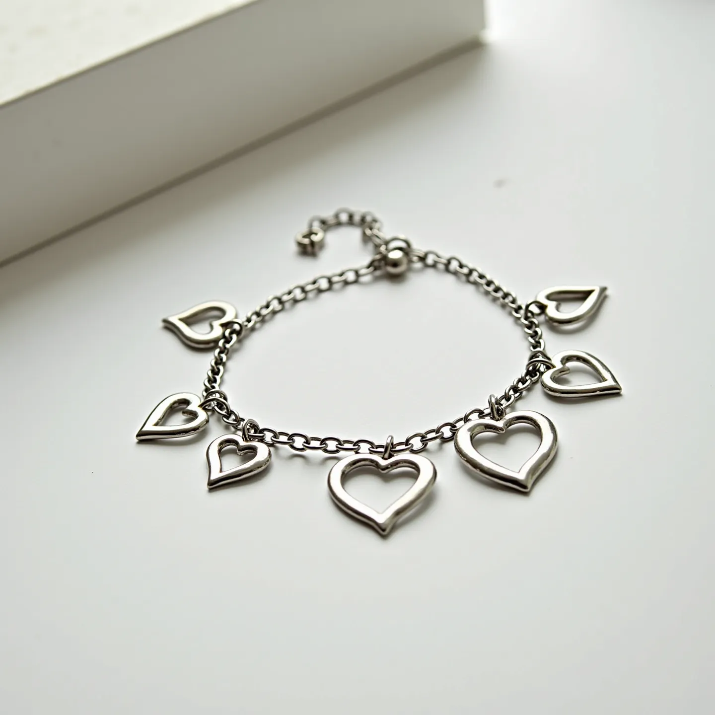 This heart bracelet features an elegant arrangement of seven heart-shaped charms made from a shiny metal, likely silver or a silver-toned material, linked by a delicate chain. Each heart charm is open in the center, exhibiting a hollow design that accentuates their minimalist aesthetic. The bracelet is equipped with an adjustable chain and a lobster clasp, ensuring a secure fit and ease of wear. The polished finish of the metal adds a touch of sophistication to this charming piece.