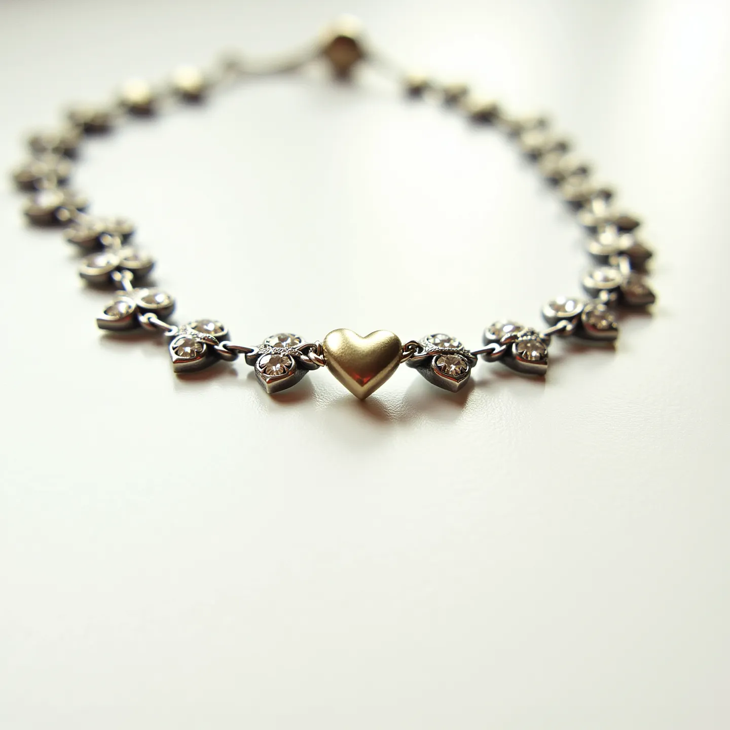 This heart bracelet features a series of linked hearts, each adorned with clear, round-cut gemstones set within the metal. At the center of the bracelet is a distinctive golden heart that stands out due to its smooth, polished finish. The gemstones are most likely cubic zirconia or diamonds, set in a prong setting to securely hold each stone in place. The bracelet is secured with a lobster clasp, providing a reliable and easy-to-use fastening mechanism.