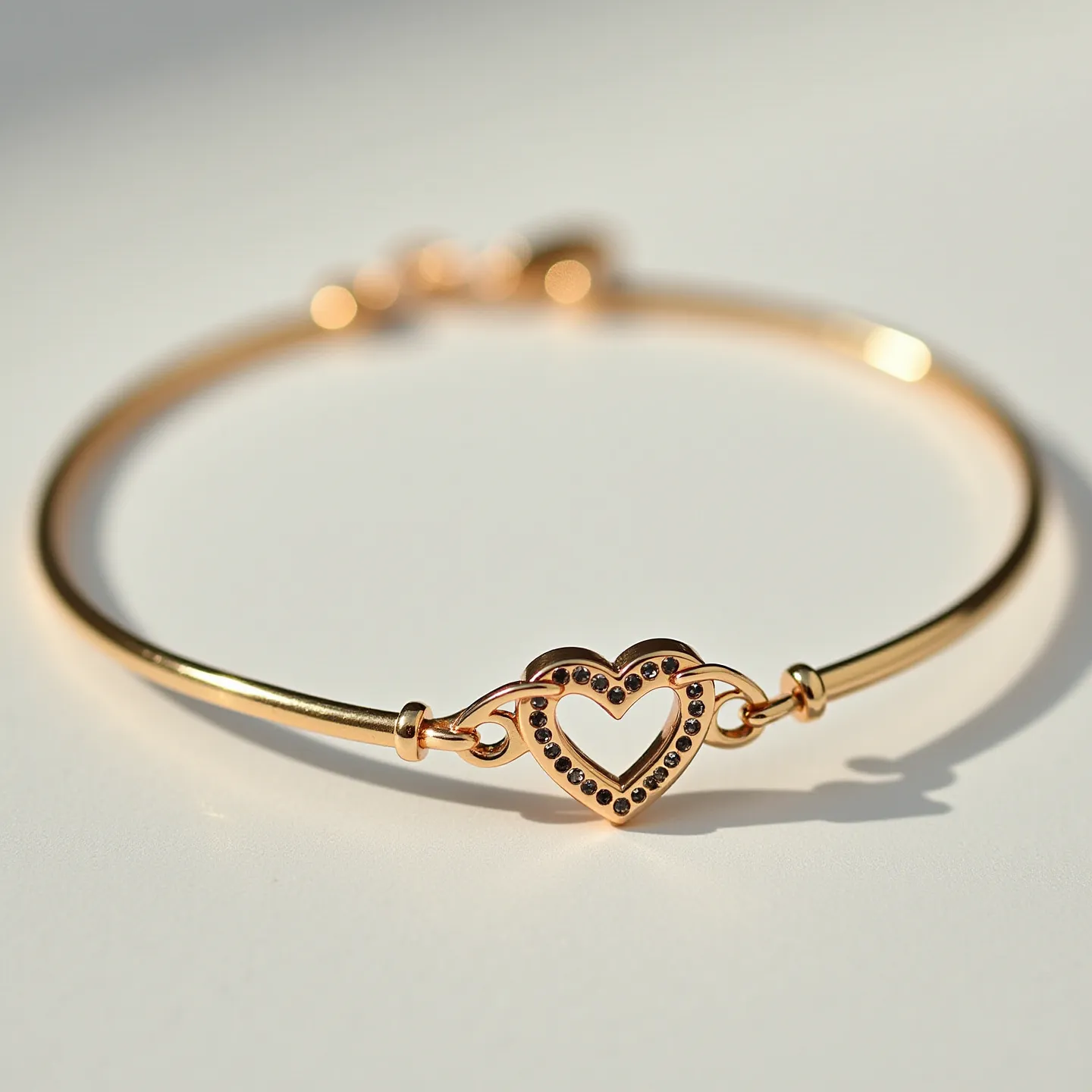 This heart bracelet features a delicate metal band with a prominent heart-shaped centerpiece. The centerpiece is adorned with small, dark-colored round stones set in a pave setting, giving it a sparkling appearance. The heart is attached to the bracelet with two small loops at the sides, integrating seamlessly into the band. The bracelet closes with a secure clasp mechanism, ensuring it remains firmly in place when worn. The metallic finish appears to be a polished gold tone, adding a touch of elegance to this piece of jewelry.