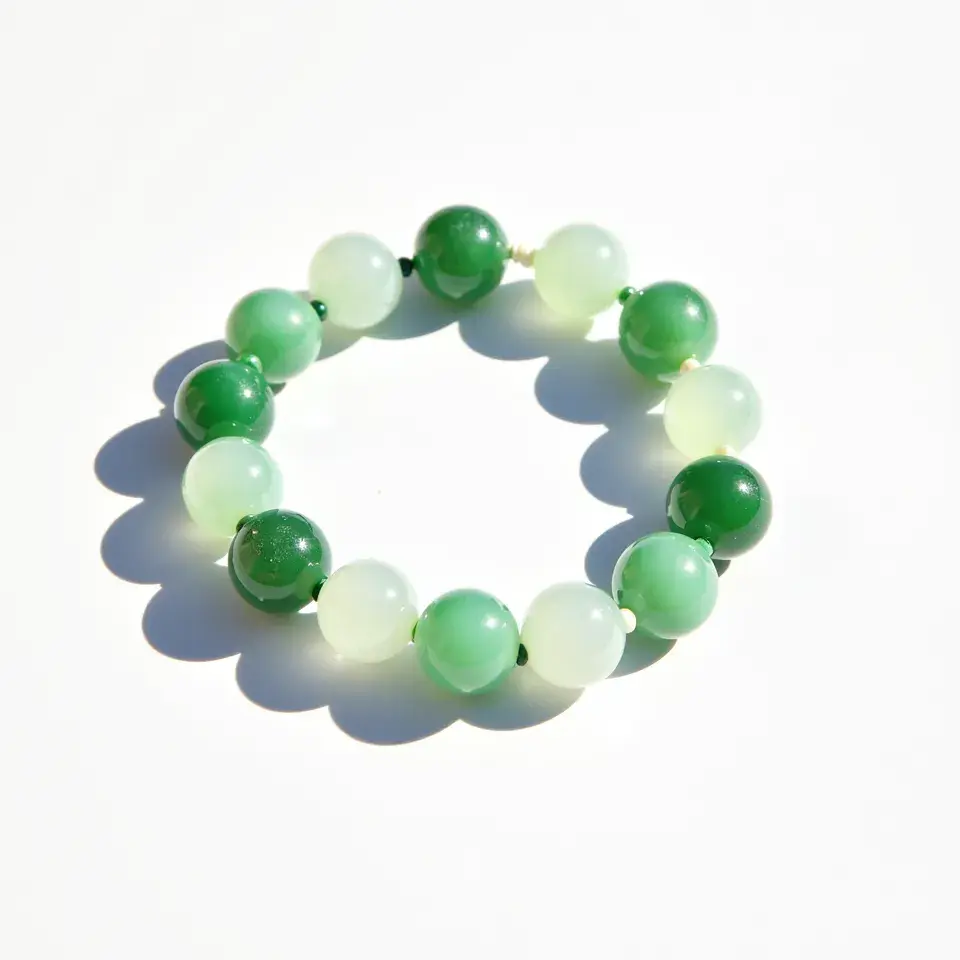 This jade bracelet is composed of polished round beads varying in shades of green, ranging from deep emerald to a lighter, more translucent green hue. The beads are strung together in a continuous loop, with no visible clasp or attachment, suggesting it is likely an elastic bracelet. The smooth, polished surface of each bead highlights the natural beauty and variations within the jade material. Each bead appears to be uniformly cut and drilled, allowing for cohesive and seamless assembly.