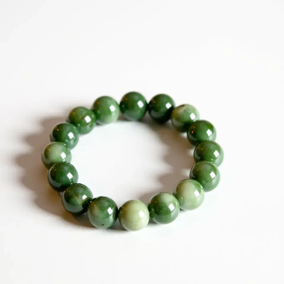 This jade bracelet features a series of uniformly round, polished jade beads of varying shades of green. The stones are smoothly polished, enhancing their natural luster and depth. There are no additional gems or elaborate settings incorporated into the design of this bracelet. The bracelet appears to be strung together on an elastic band, which allows for flexibility and ease of wearing without the need for a traditional clasp or closure.