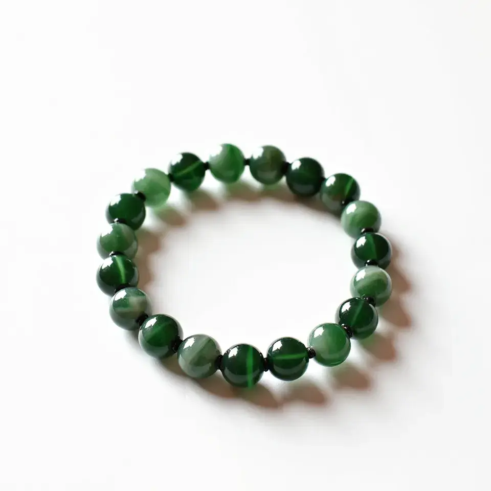 This jade bracelet features a collection of polished, spherical jade beads arranged in a continuous loop. The beads exhibit a rich green color with subtle variations in shading, highlighting the natural beauty of the jade material. Each bead is smoothly cut and polished to a glossy finish, enhancing the overall elegance. The beads are likely threaded together on an elastic cord, allowing for a flexible and comfortable fit without the need for a clasp or attachment. The simplicity of the design emphasizes the quality and allure of the jade stones.