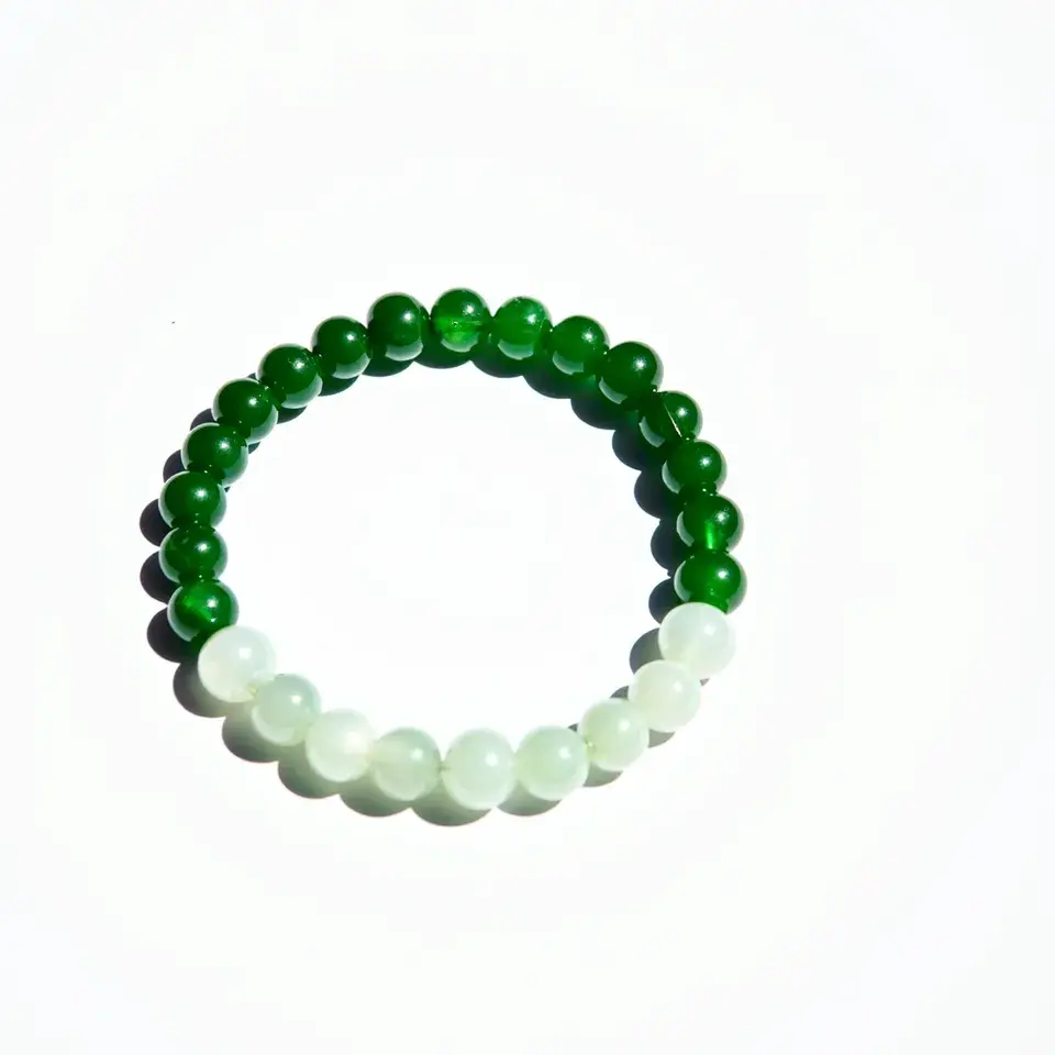 This jade bracelet is composed of smooth, round jade beads, alternating in color from a rich green to a milky white. The beads are strung together tightly, forming a continuous loop without any visible clasp or attachment, suggesting an elastic or stretchable string for easy wear. The green and white jade stones are polished to a high shine, enhancing their natural luster and vibrant hues.