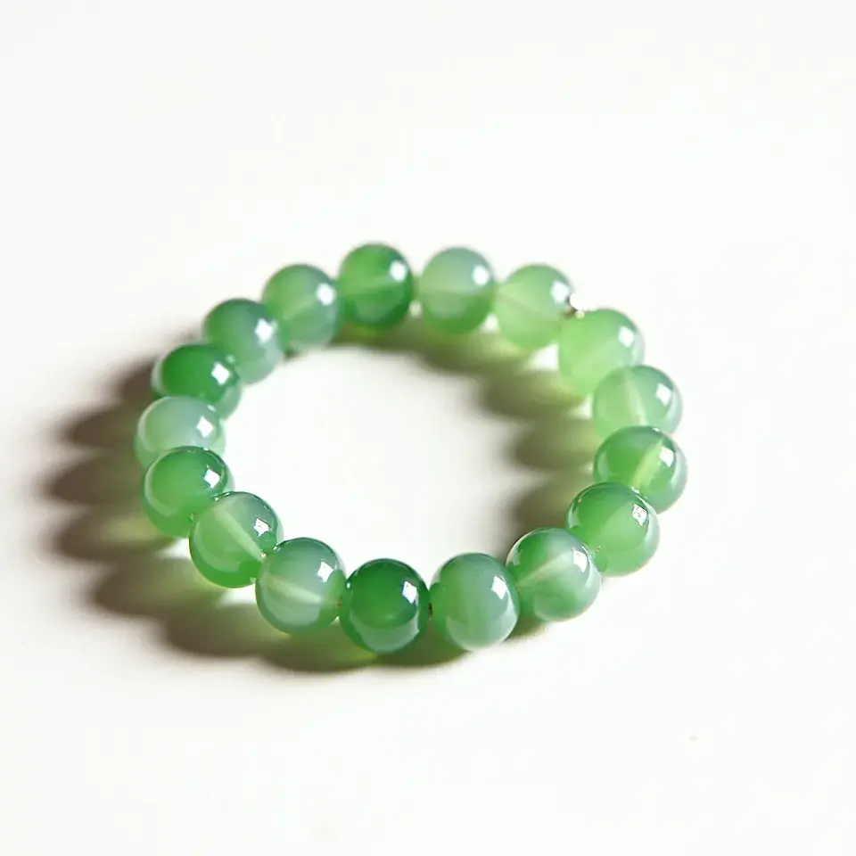 This jade bracelet features a series of round jade beads, each with a polished finish that highlights the natural green hues of the stone. The beads are uniform in size and are strung together in an elastic or flexible band style, allowing for a seamless and continuous circular form. There are no additional gems, intricate cuts, or specific settings on the beads, emphasizing the inherent beauty of the jade itself. The bracelet does not appear to have a clasp or other attachment, relying on its stretchable design for ease of wear.