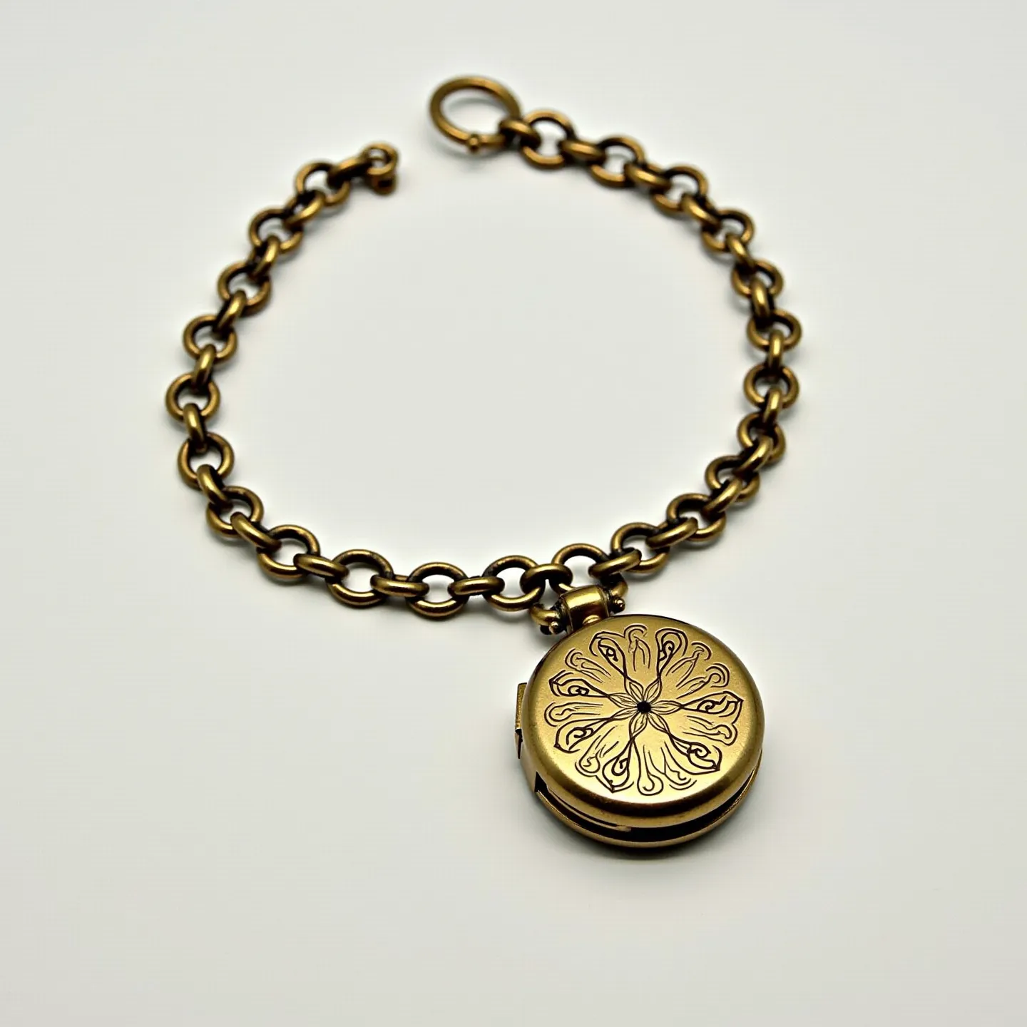 This locket bracelet features a circular locket pendant suspended from a chain of interconnected metal links, which appear to be made of a bronze or antique gold material, giving it a classic and vintage look. The front of the locket is adorned with an intricate engraved design resembling a flower or ornate pattern. The bracelet is secured with a round metal clasp that complements the overall cohesive aesthetic.