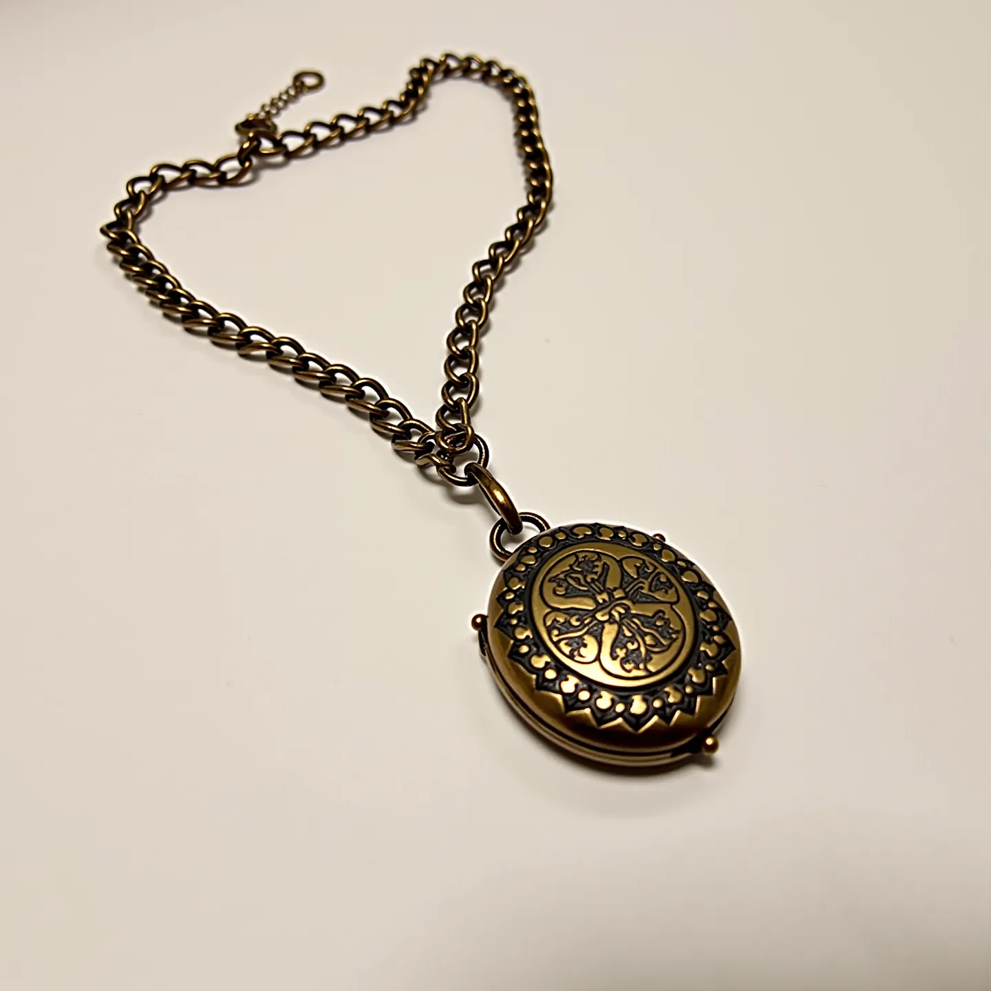 This locket bracelet features a vintage design, composed of a metal chain and an intricately detailed locket. The bracelet's chain is made of interlinked rounded metal loops, ensuring durability and style. The focal point of the bracelet is the oval-shaped locket, which is adorned with a detailed floral or ornate pattern on its front lid, set within a decorative border. The locket's hinge and clasp mechanism appear sturdy and functional, allowing for keepsakes to be safely stored inside. The bracelet is secured with a classic lobster clasp, providing a reliable fastening method. 