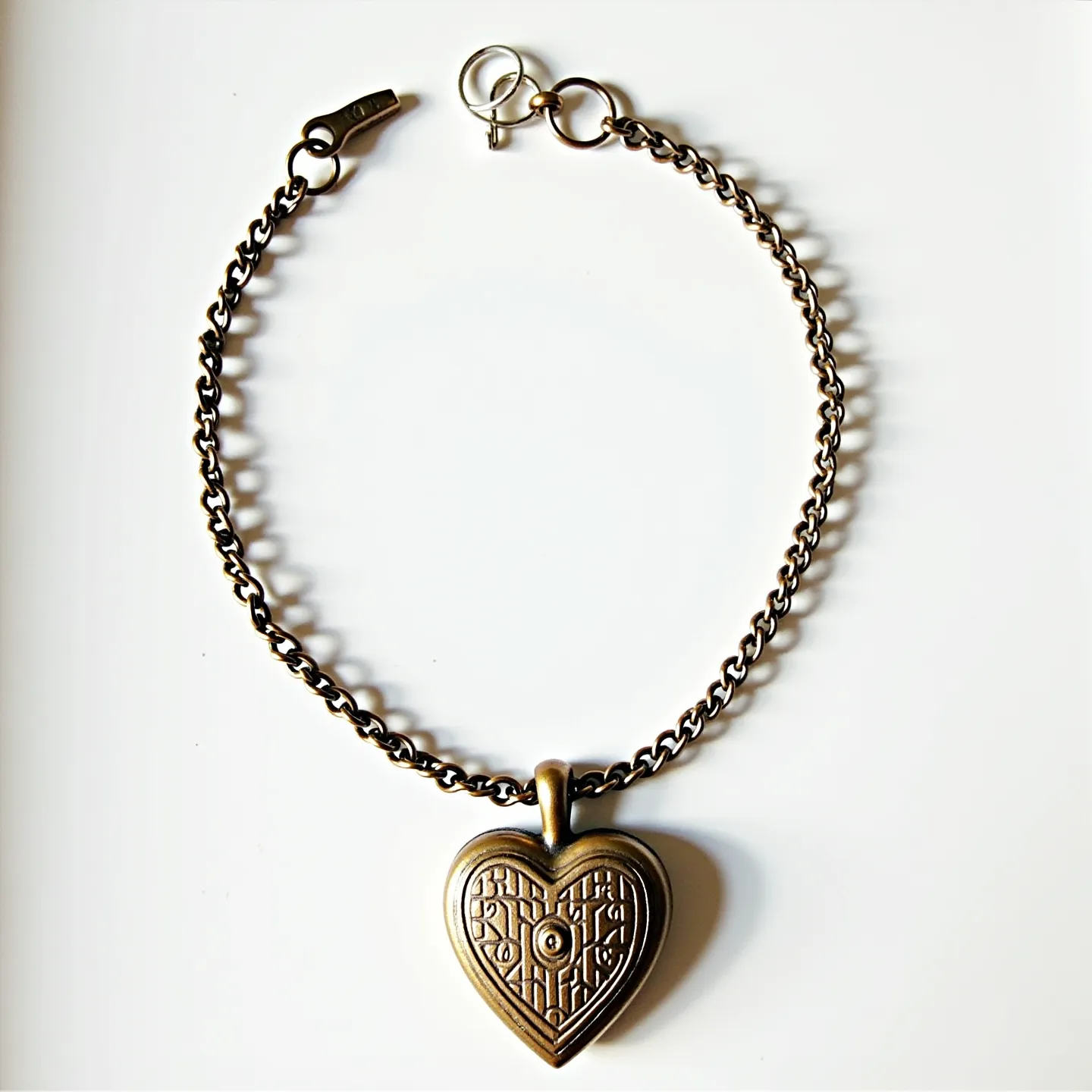 This locket bracelet features a sturdy, metallic chain, likely made from brass or a similar alloy, giving it a classic and timeless appearance. The centerpiece is a heart-shaped locket with intricate geometric patterns etched onto its surface, suggesting a blend of vintage and modern design elements. The locket is securely attached to the chain with a robust bail that ensures it stays in place. The bracelet is closed with a lobster clasp, providing a secure and easy-to-use mechanism to wear the accessory. This locket bracelet combines elegance with sentimental value, making it a thoughtful and stylish piece of jewelry.