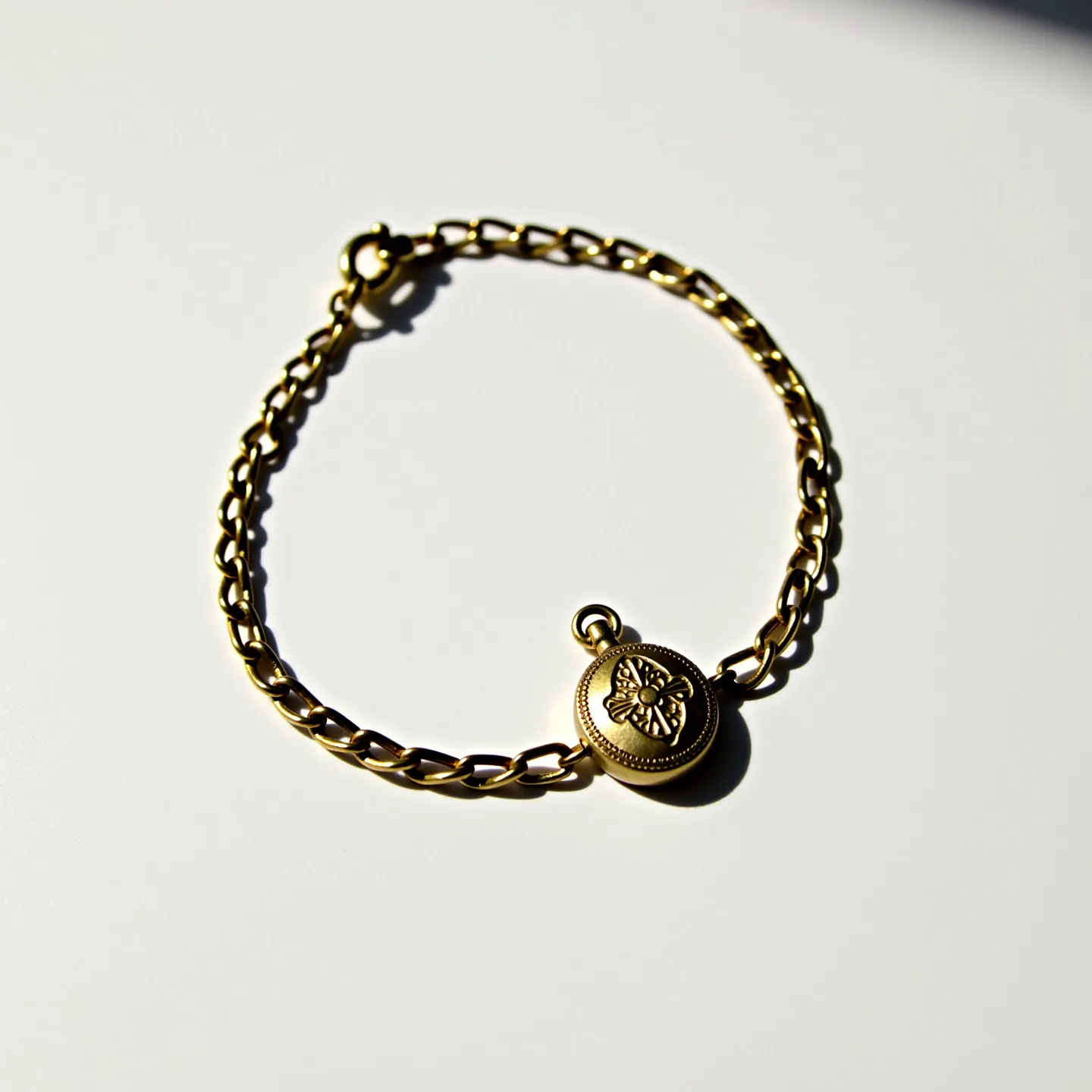 This locket bracelet features a delicate gold-tone chain composed of interlinked, polished links which give it a refined and elegant appearance. At its center, a small round locket is exquisitely designed with a floral motif etched onto its surface, adding a vintage charm to the piece. The locket's round shape is complemented by a simple hinge mechanism for opening and a small loop at the top for attachment to the chain. The bracelet is secured with a sturdy lobster clasp, ensuring it remains fastened securely during wear. This piece combines both aesthetic appeal and functional elements, making it a graceful accessory.