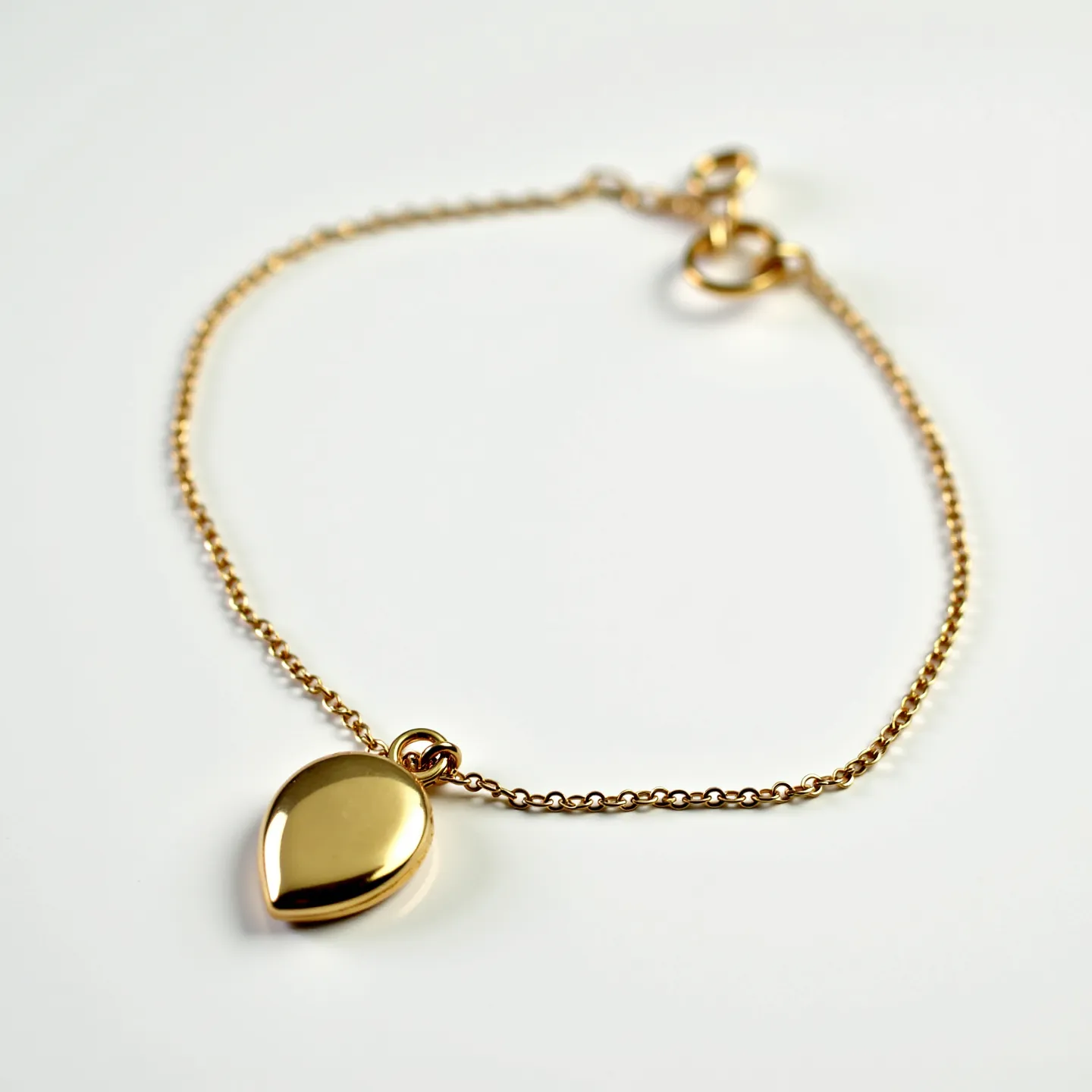 This locket bracelet features a delicate chain crafted from a gold-colored metal, seamlessly joined to a teardrop-shaped locket. The locket, also designed from the same gold-colored metal, exudes a polished and smooth finish, giving it a sleek, elegant appearance. The bracelet is completed with a secure clasp, which appears to be a spring ring type, ensuring that the piece stays securely fastened when worn. The overall design combines simplicity and elegance, making it a versatile accessory for various occasions.