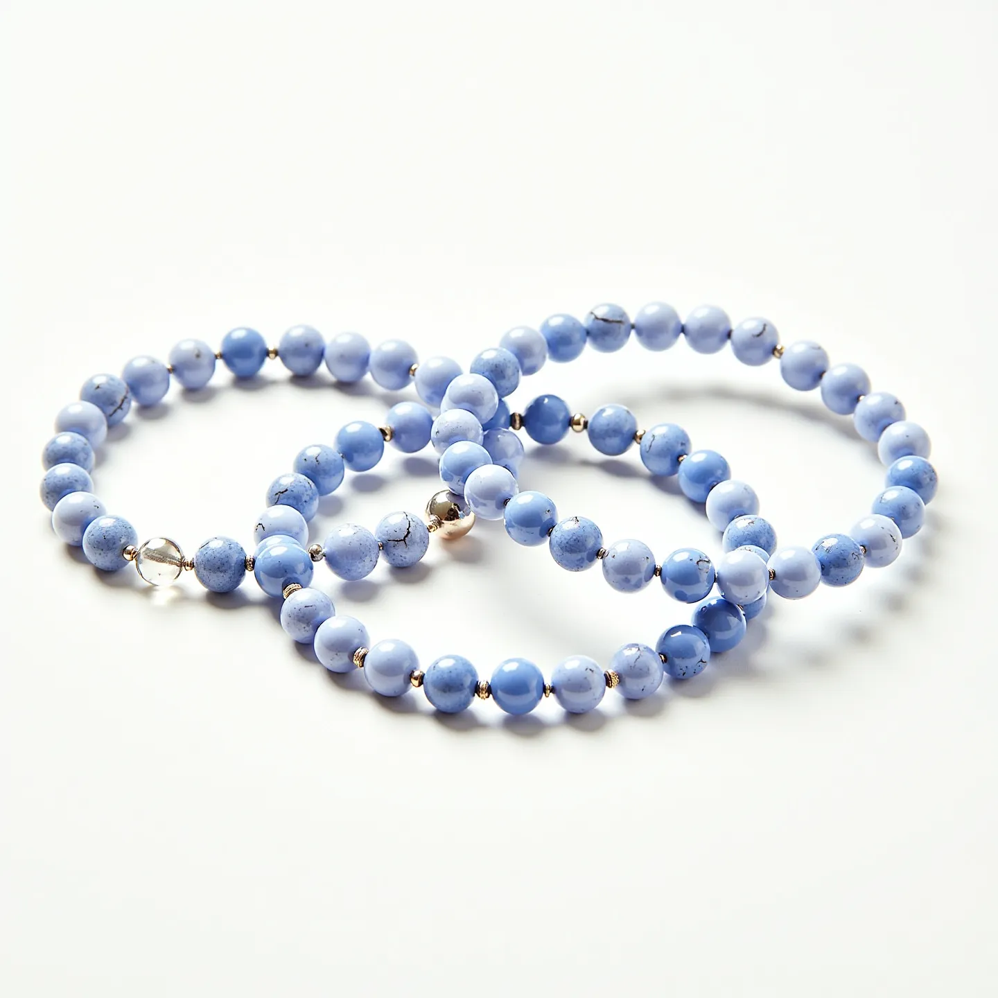 These matching bracelets each feature a series of round blue beads, likely made from a polished blue stone or dyed material, arranged in a uniform pattern. Interspersed between the blue beads are smaller metallic spacer beads which add a touch of shine and contrast. The bracelets are closed with a sturdy yet simple clasp mechanism, ensuring they stay secure when worn. The overall design is both attractive and practical, offering a harmonious blend of color and texture.