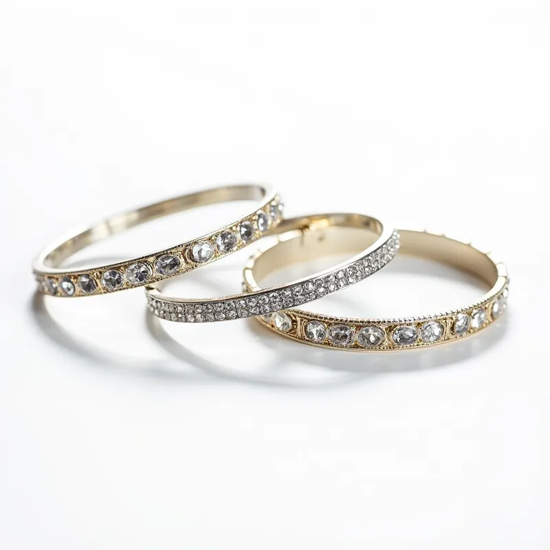 This matching bracelet set features a design centered around intricate use of metal and gemstones. Each bracelet appears to be crafted from a metal base that is delicately plated in either gold or silver tones. The primary decorative elements are the gemstones, which are clear and likely imitation diamonds or cubic zirconia, set in round, bezel settings running continuously around the band. One of the bracelets is further embellished with a row of small, pave-set stones, giving it an added layer of sparkle and shine. The clasp on one of the bracelets ensures a secure fit when worn.