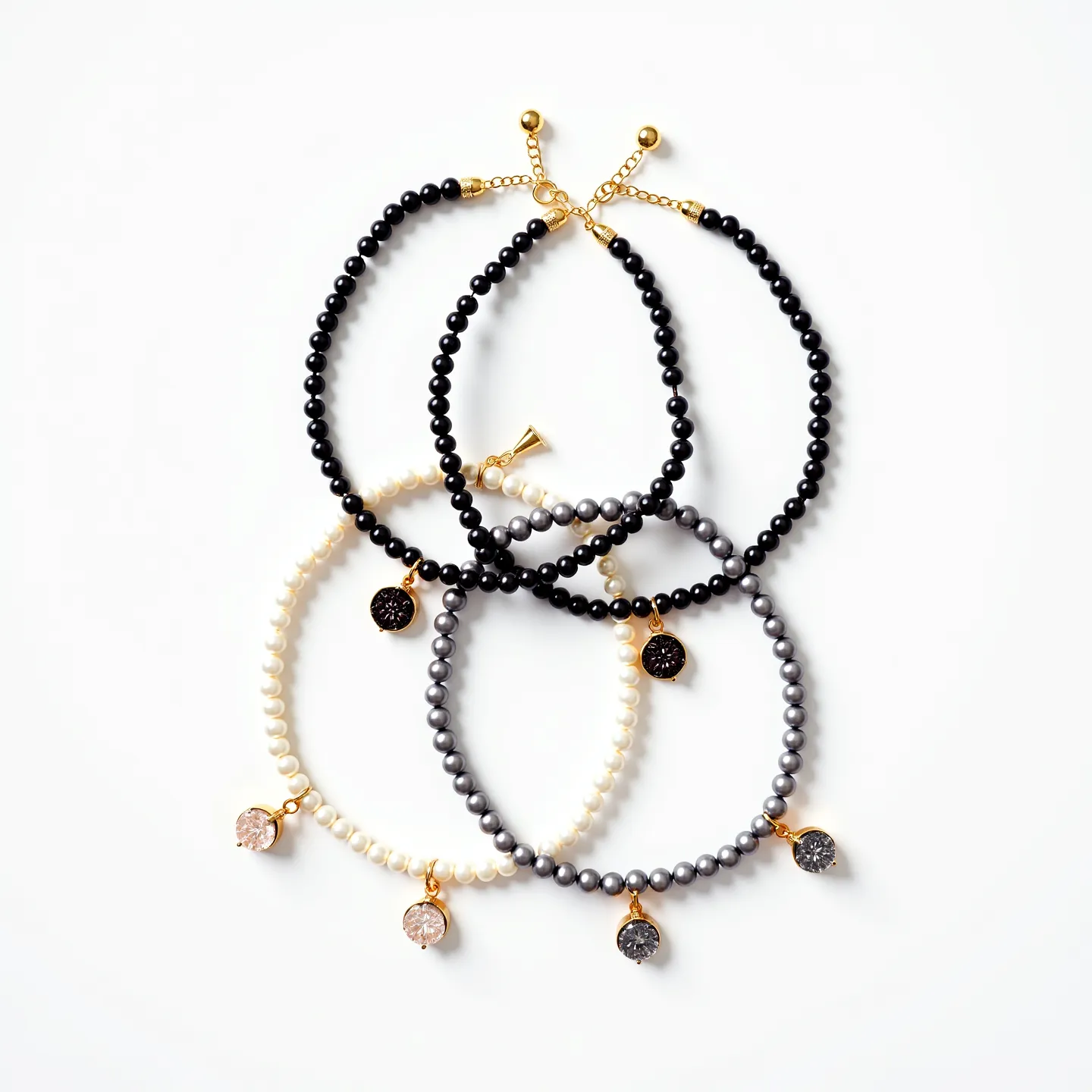 This matching bracelets set features four distinct designs made from various beads. Each bracelet showcases differently colored round beads—black, white, grey, and another black bead strand. Attached to each strand is a single hanging charm with a distinctive stone that appears to be a round-cut gem set in a pronged gold-colored setting. The stones vary in color, complementing the bracelets' beads. The clasps are gold-colored with adjustable chain extensions, ensuring a secure and customizable fit. The use of gold accents combined with the beads and stone settings create a cohesive and elegant look.